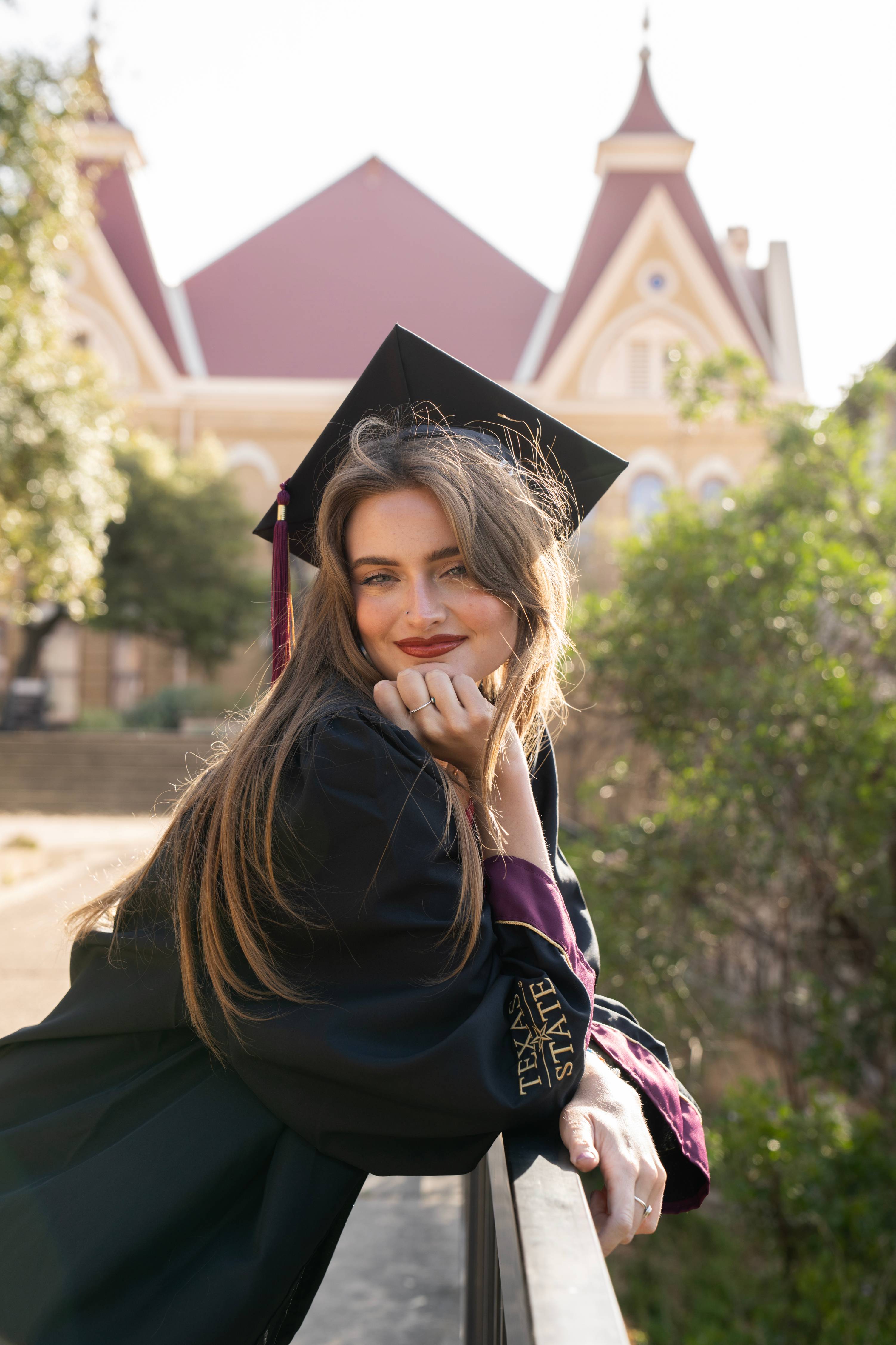 Close up of a graduate leaning against the railing near Old Main, smiling at the camera