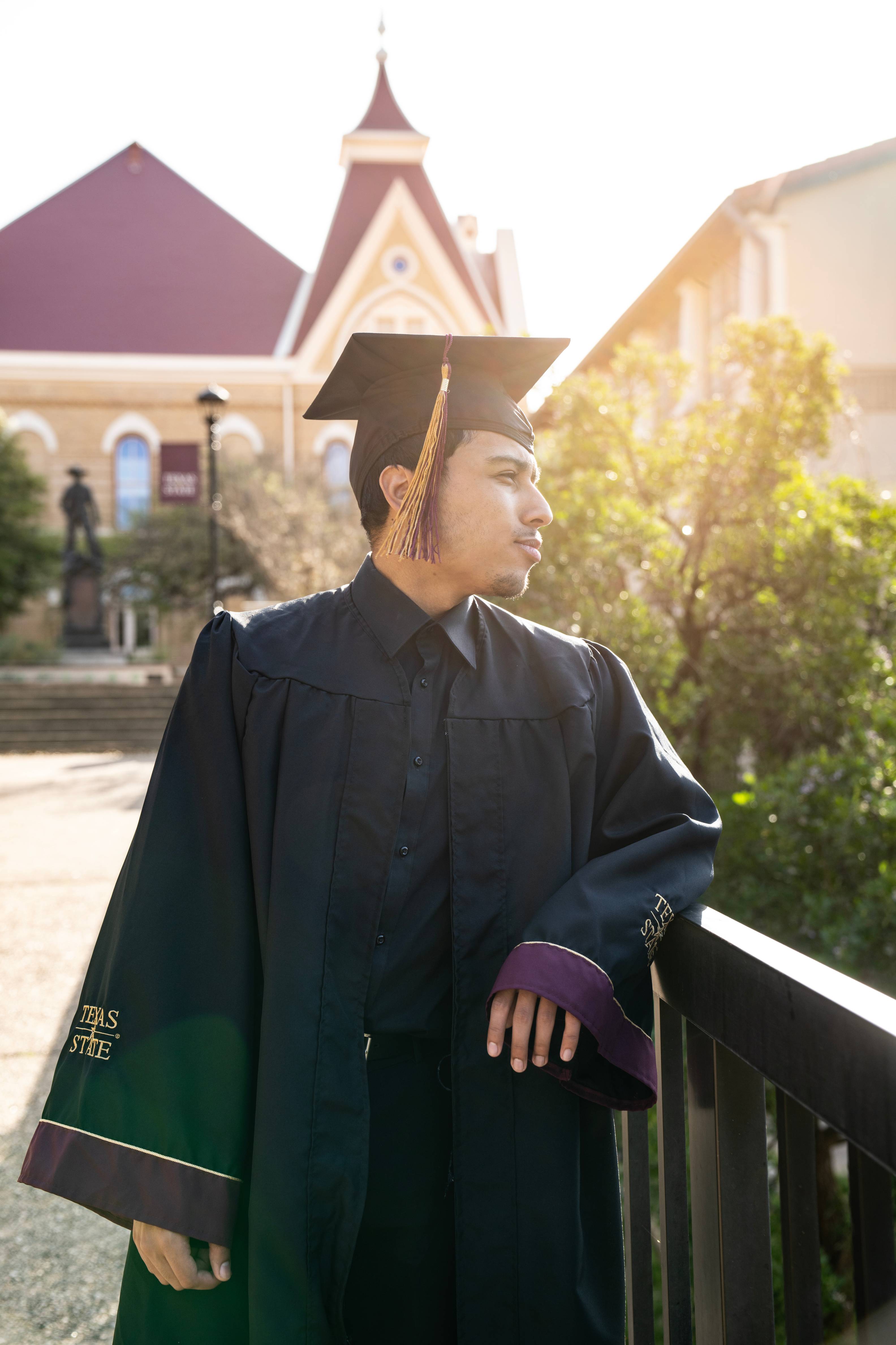 Close up of a graduate leaning against the railing near Old Main, looking off to the side