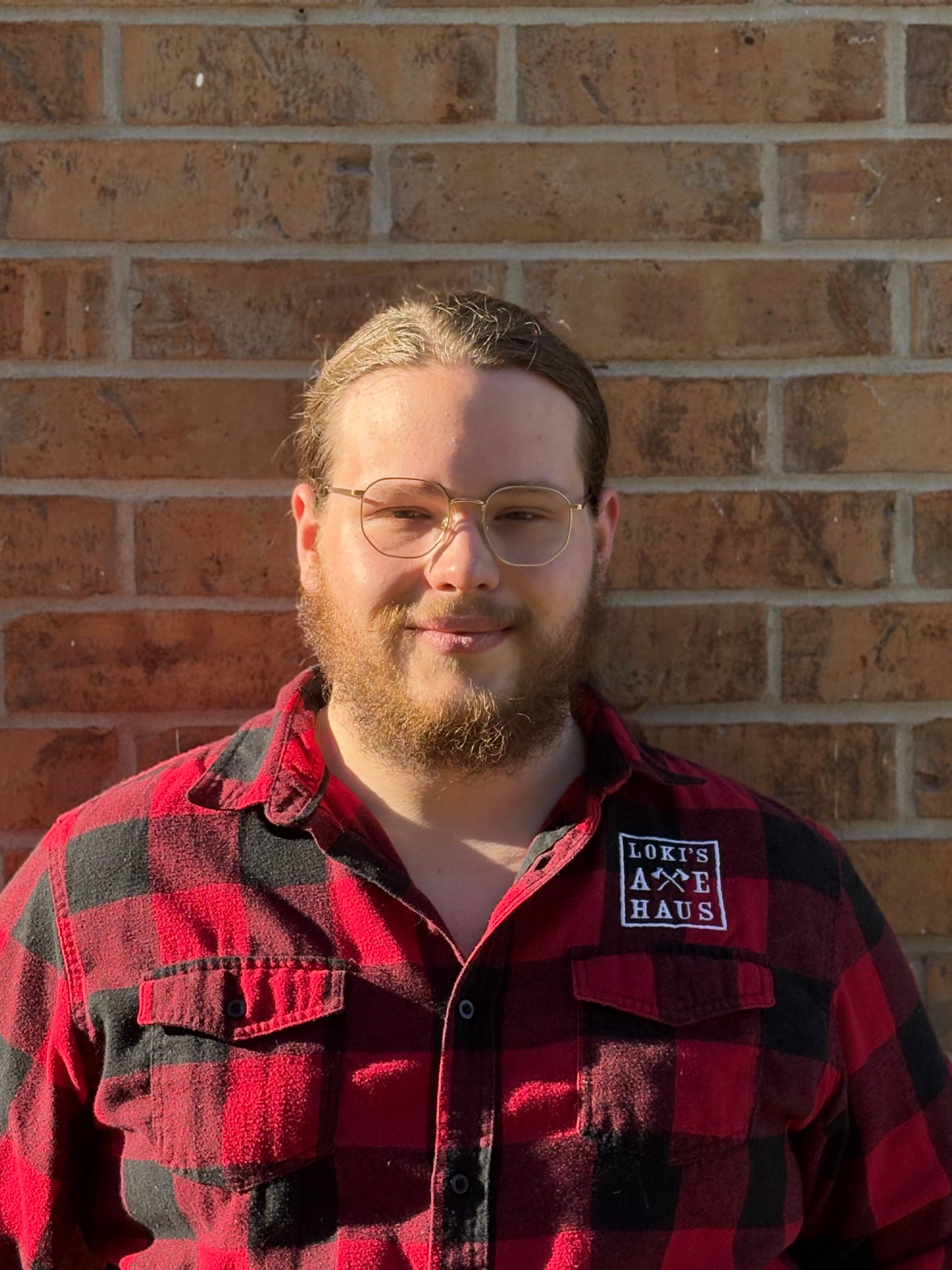 man wearing flannel shirt in front of brick wall