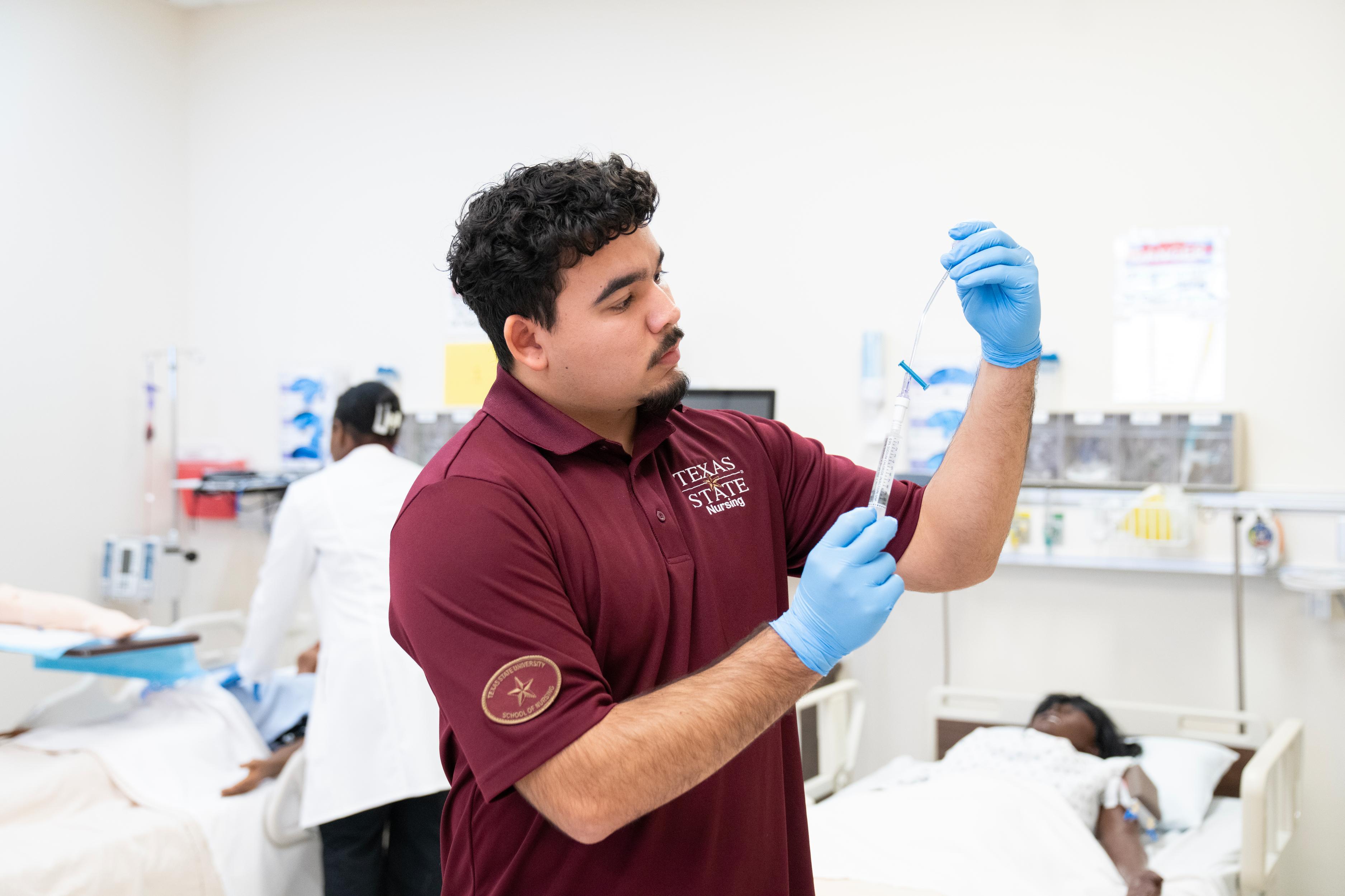 male nursing student looking at plastic tubing while wearing blue nitrile gloves