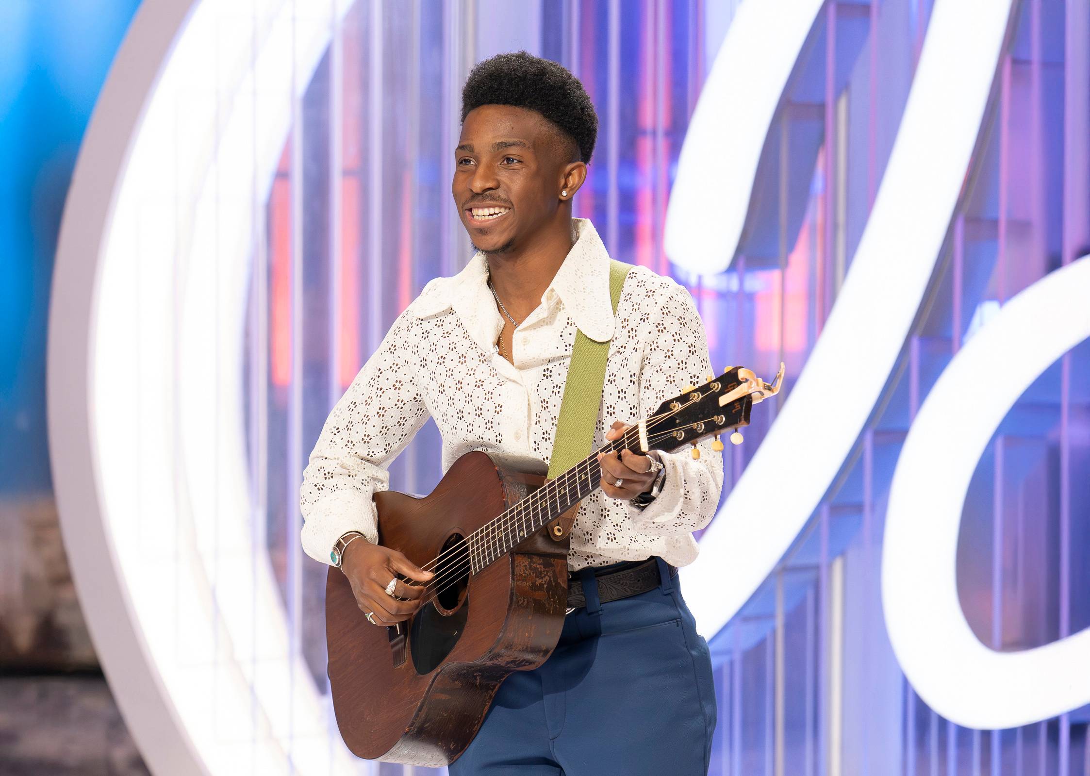 man smiles and plays acoustic guitar while auditioning for American Idol