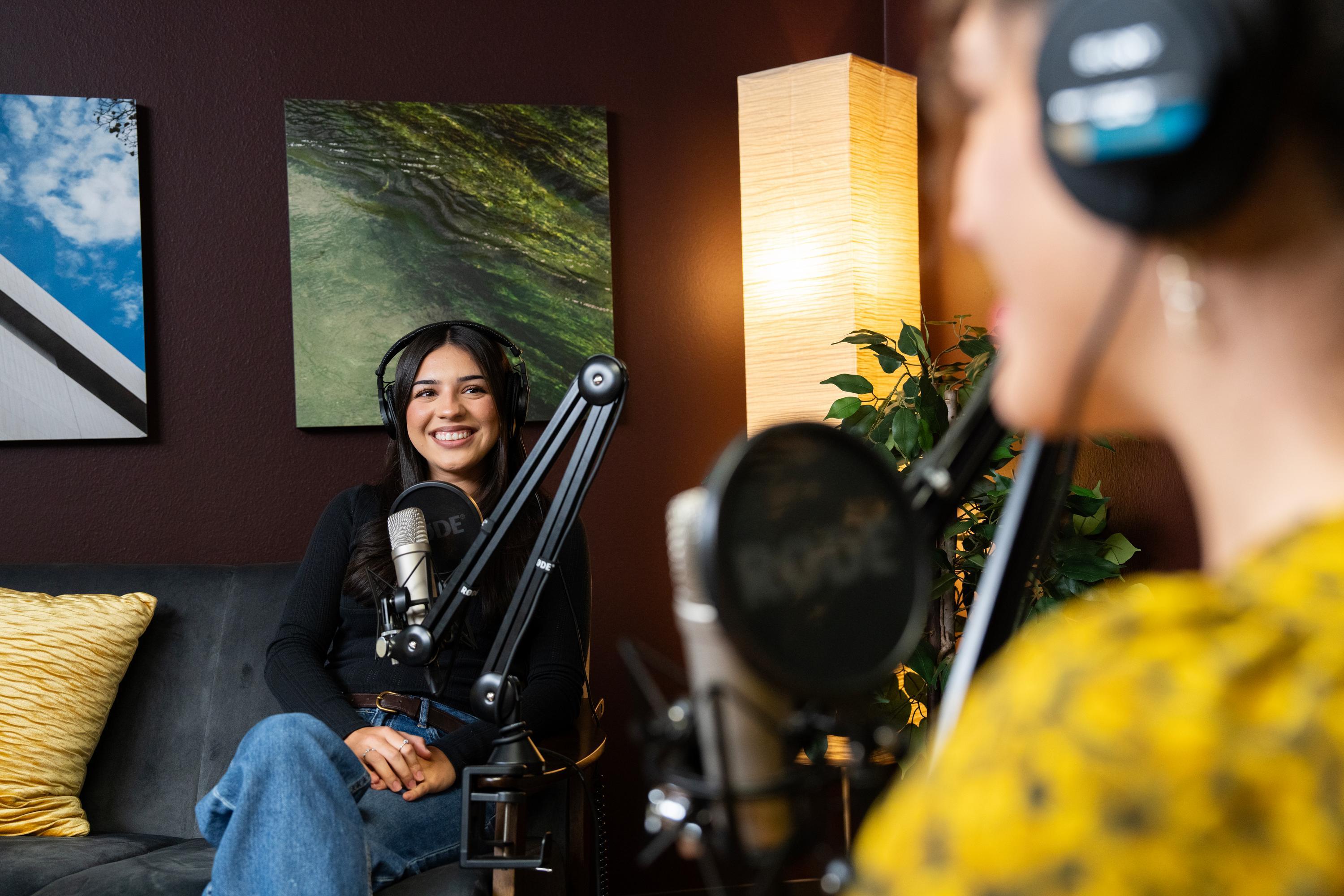 two women wearing headphones and sitting in front of mics in a podcast studio