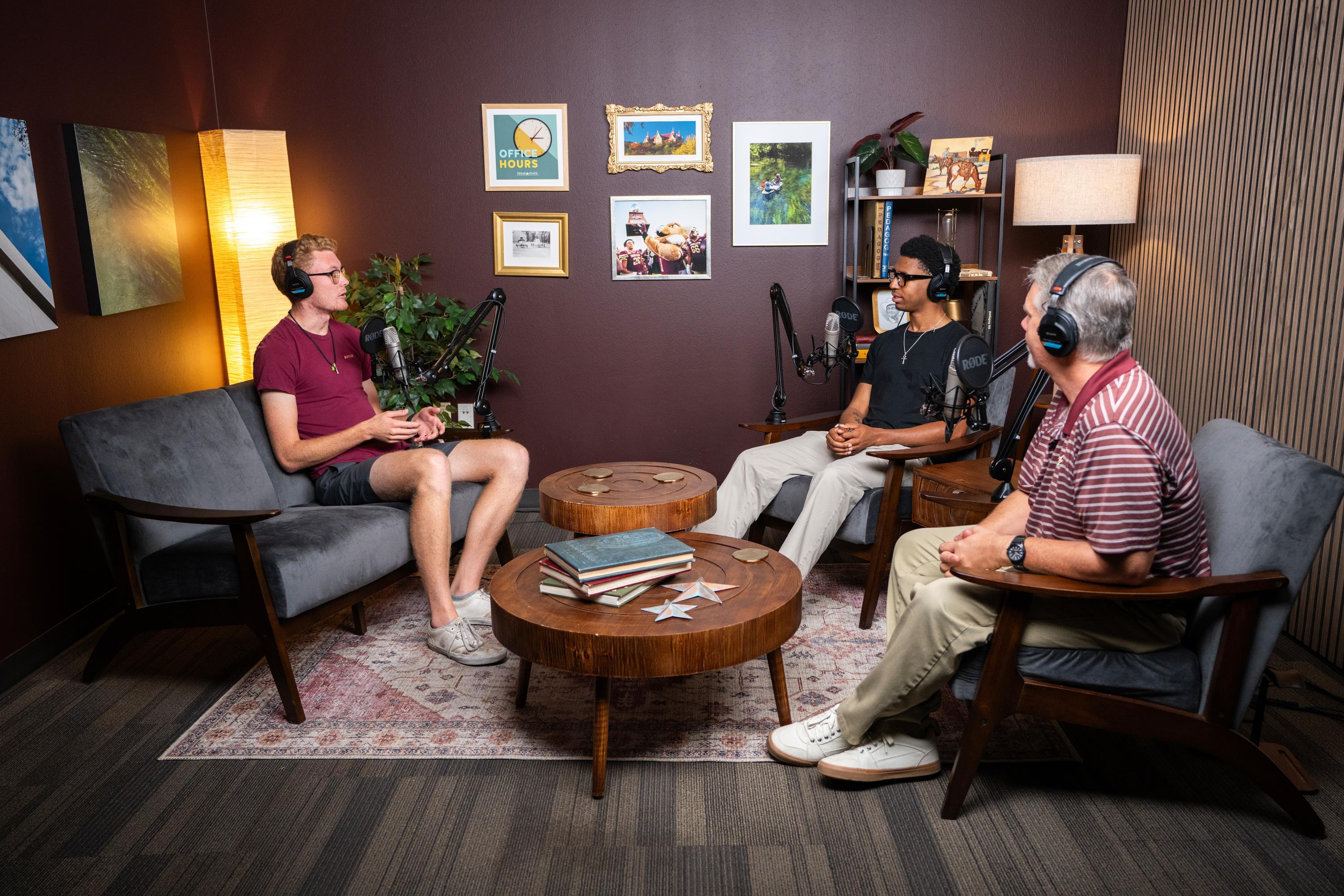 three men sit in front of microphones in a podcast studio with headphones on 