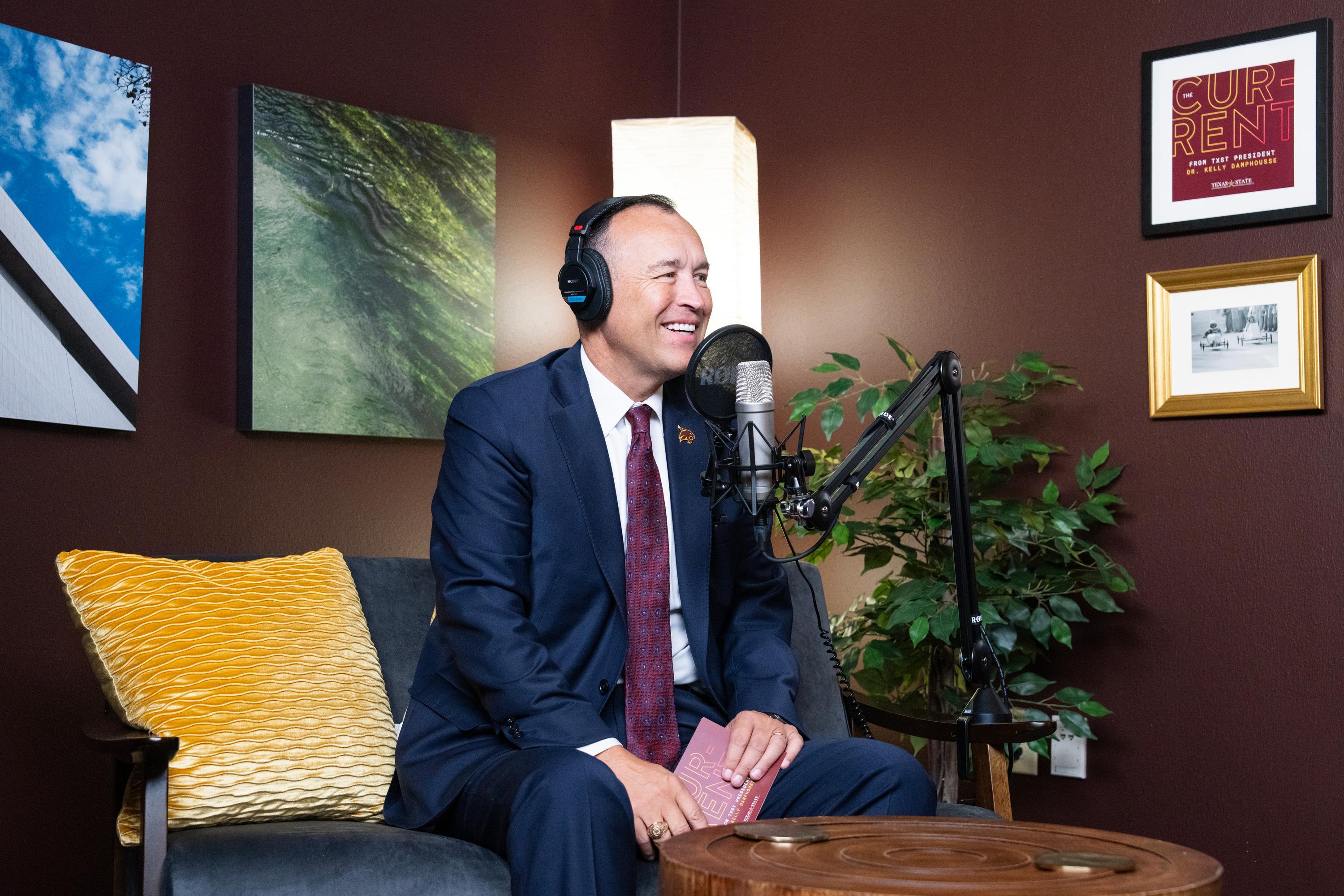 President Kelly Damphousse wearing headphones and smiling in front of a microphone