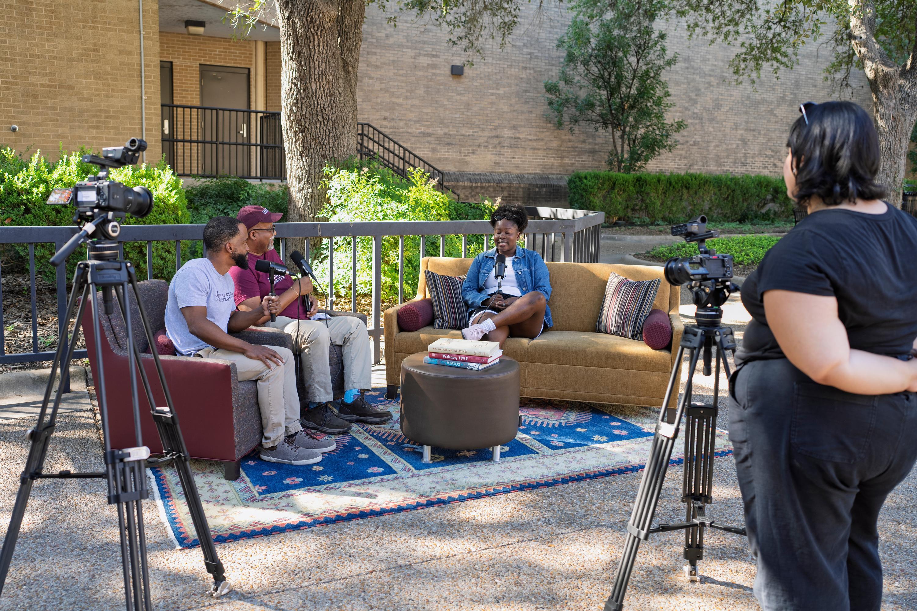 a woman films three people recording a podcast on couches outside