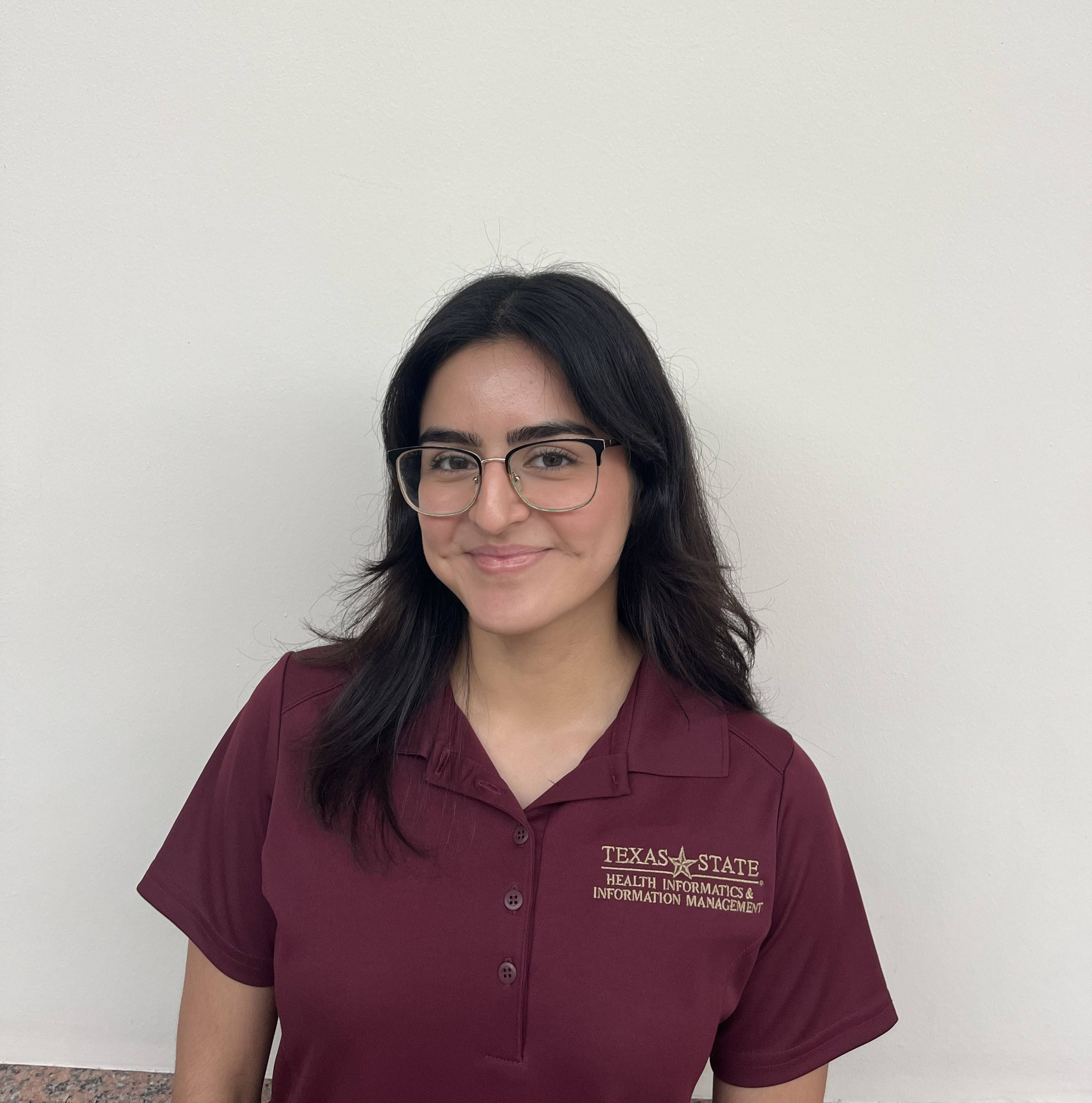 Student in a maroon shirt standing against a blank wall.