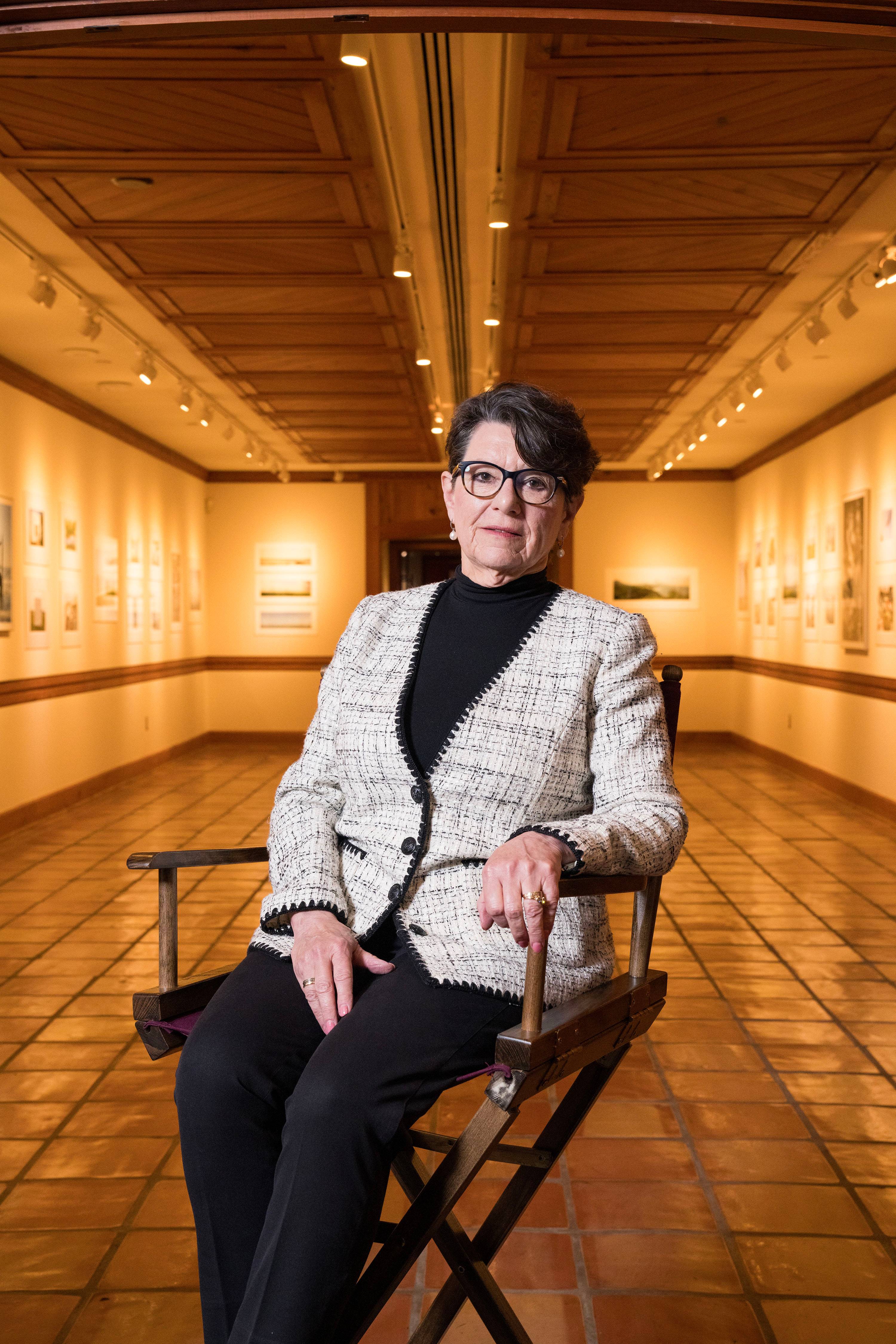 Marise McDermott sitting in a directors chair in a gallery at the Wittliff Collections