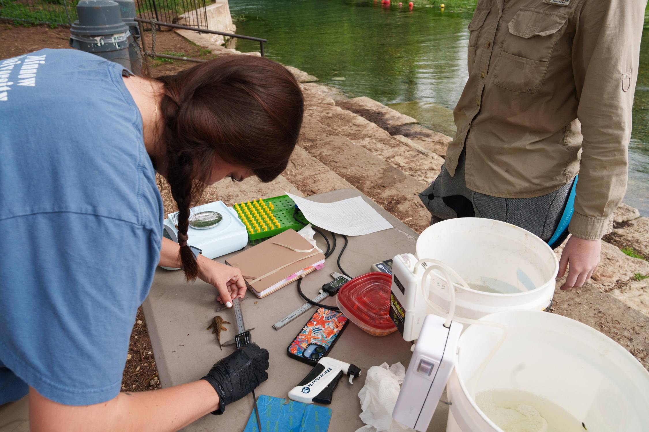 woman measuring a small fish on a table near a river bank