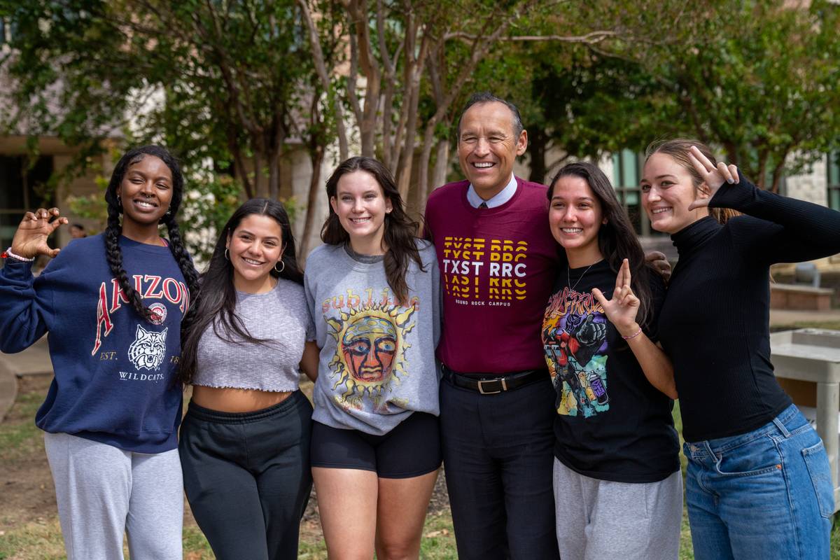 President Kelly Damphousse with several female students posing for a group picture