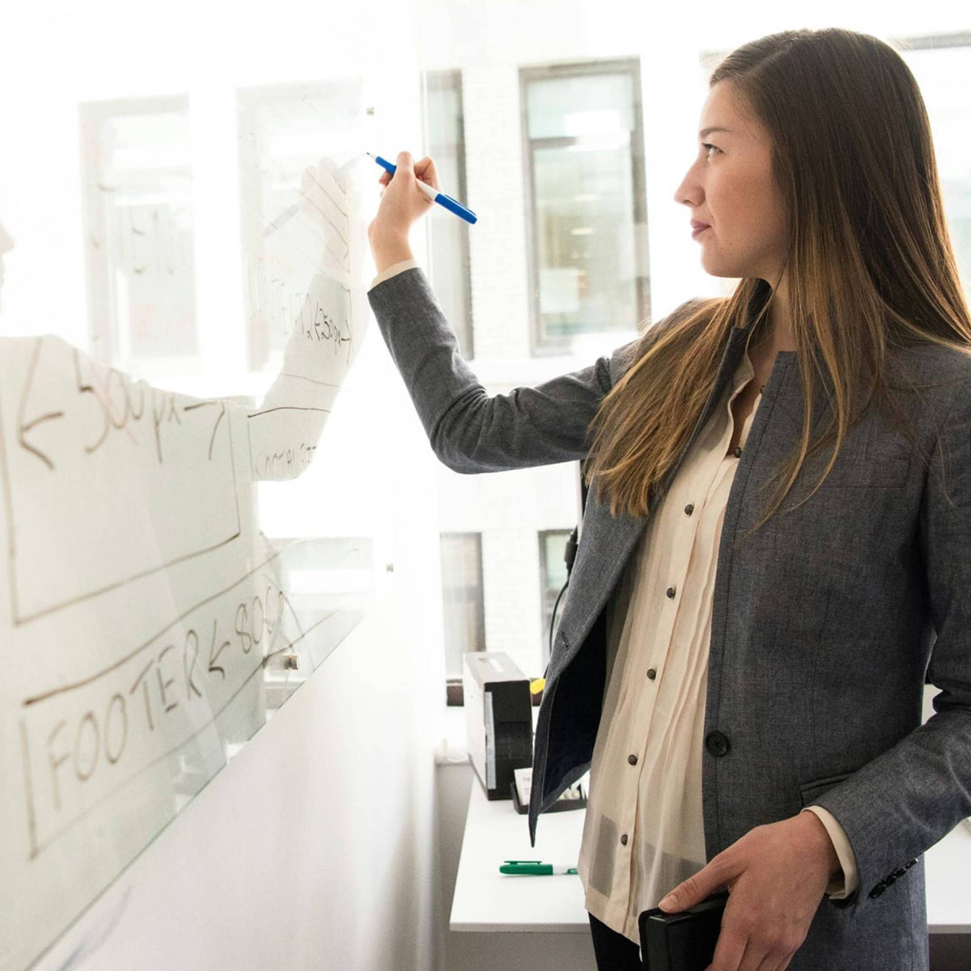 woman in professional attire writing on white board