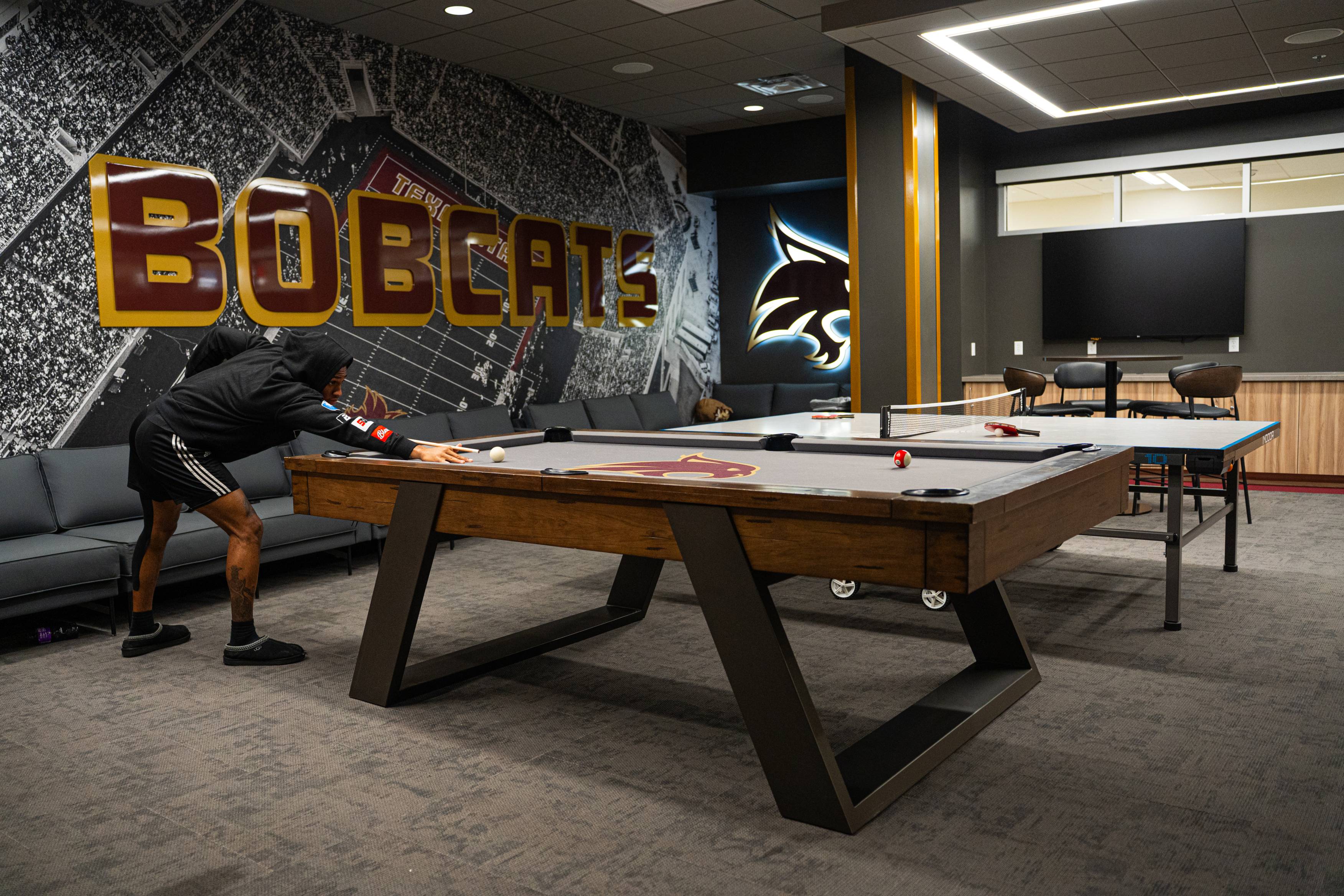 football player playing billards in TXST Bobcats themed lounge