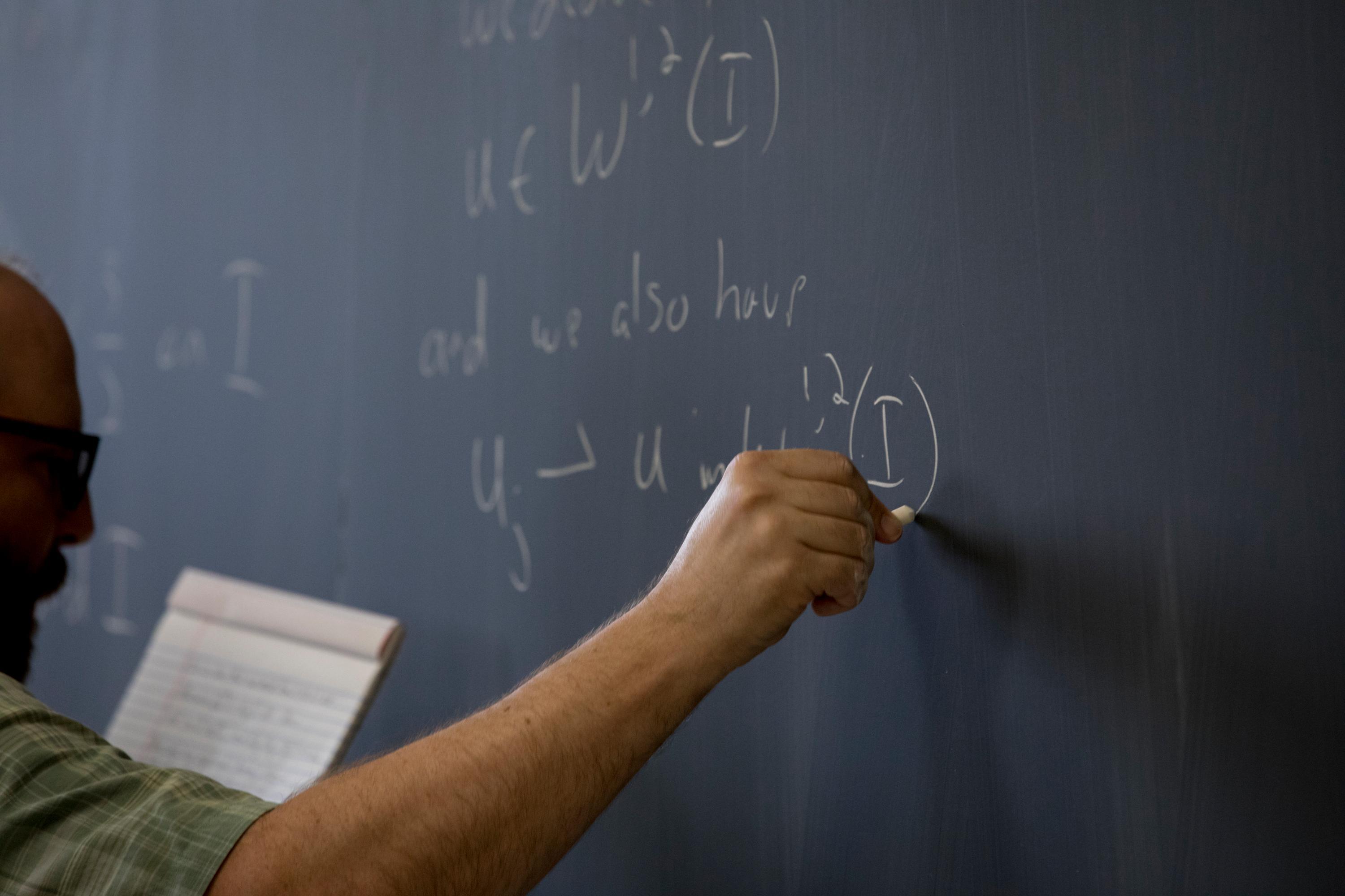 man writing on black chalkboard 