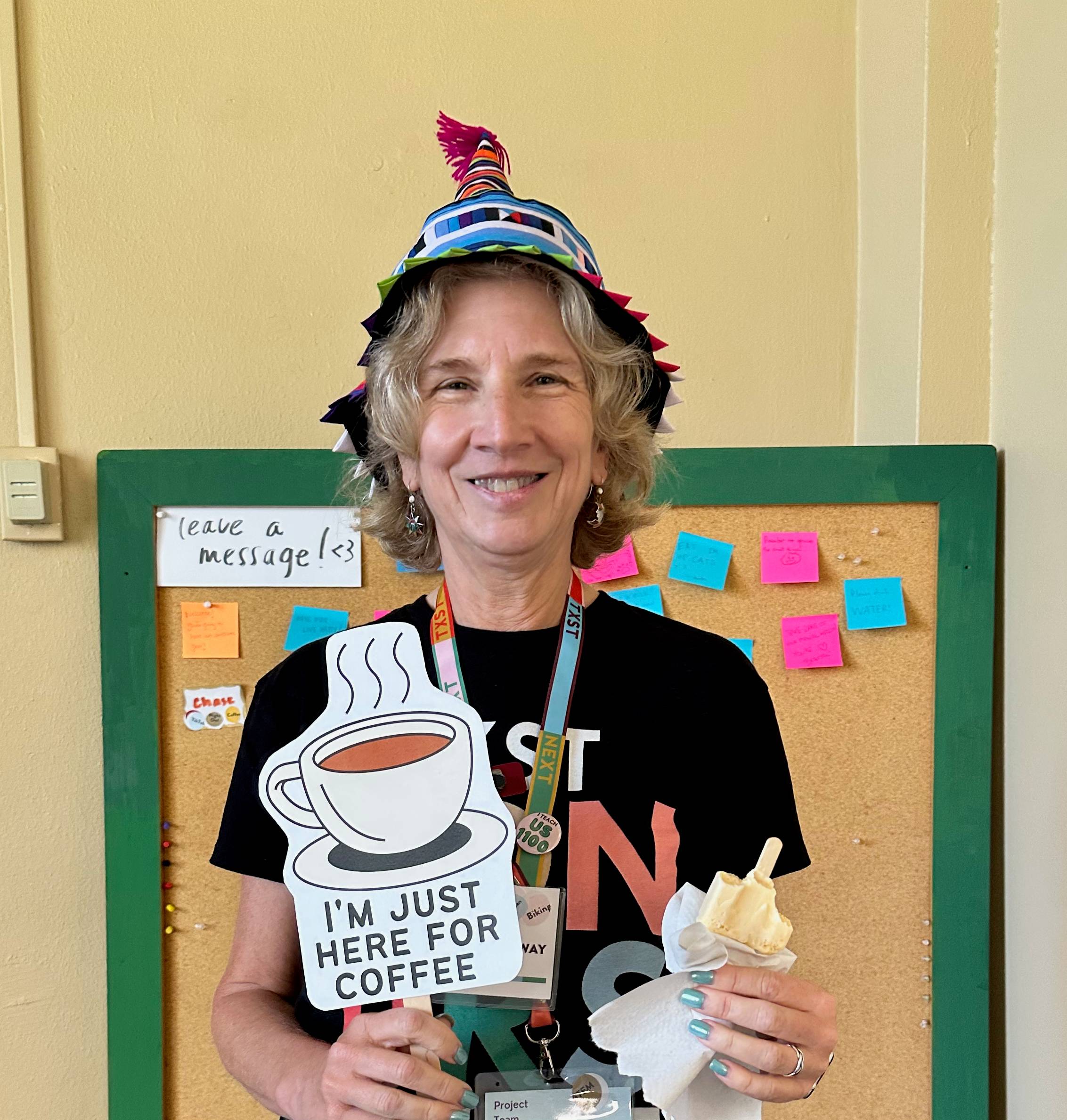 woman holds up a sign that reads "i'm just here for the coffee" while wearing a silly hat