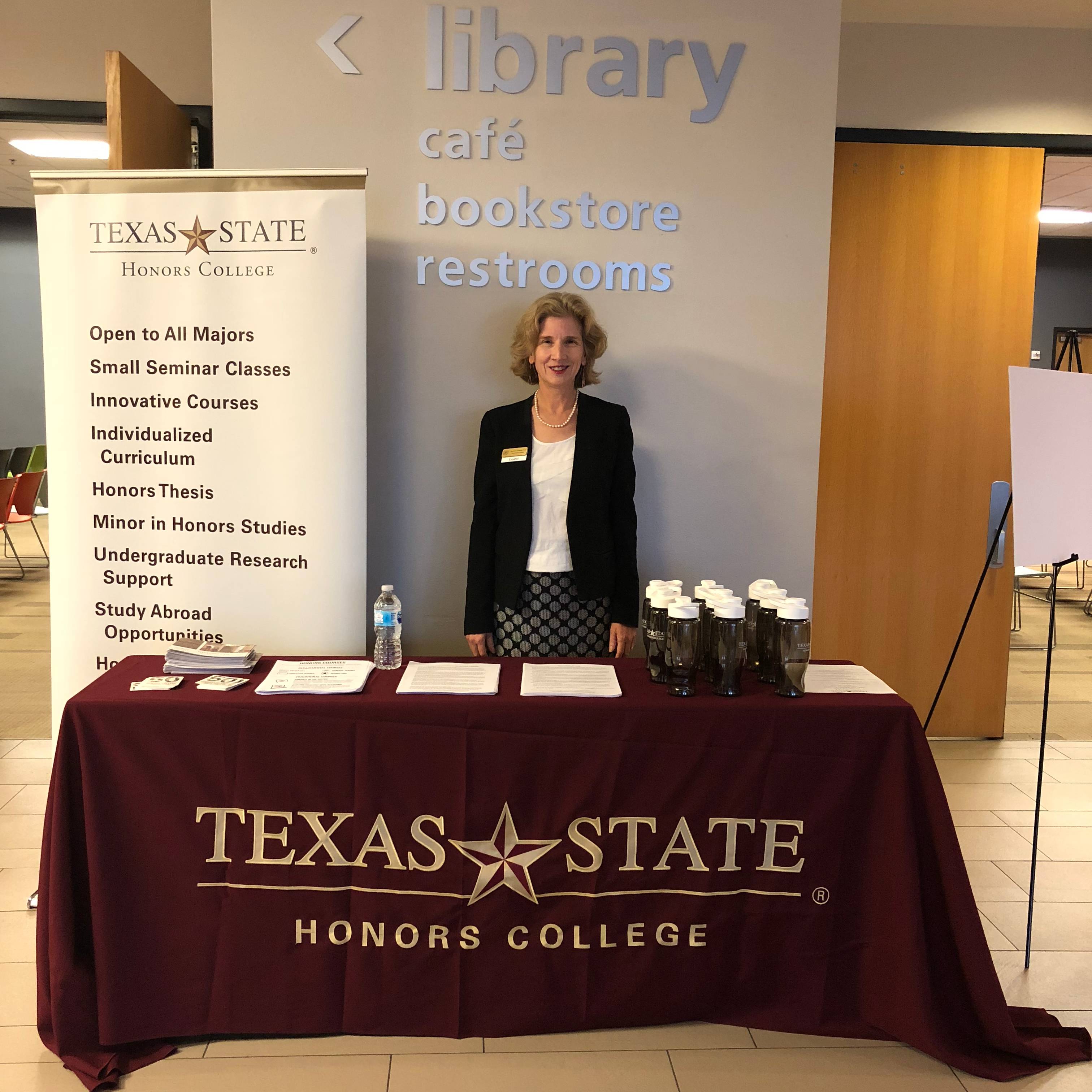 woman stands behind table that reads "texas state honors college"