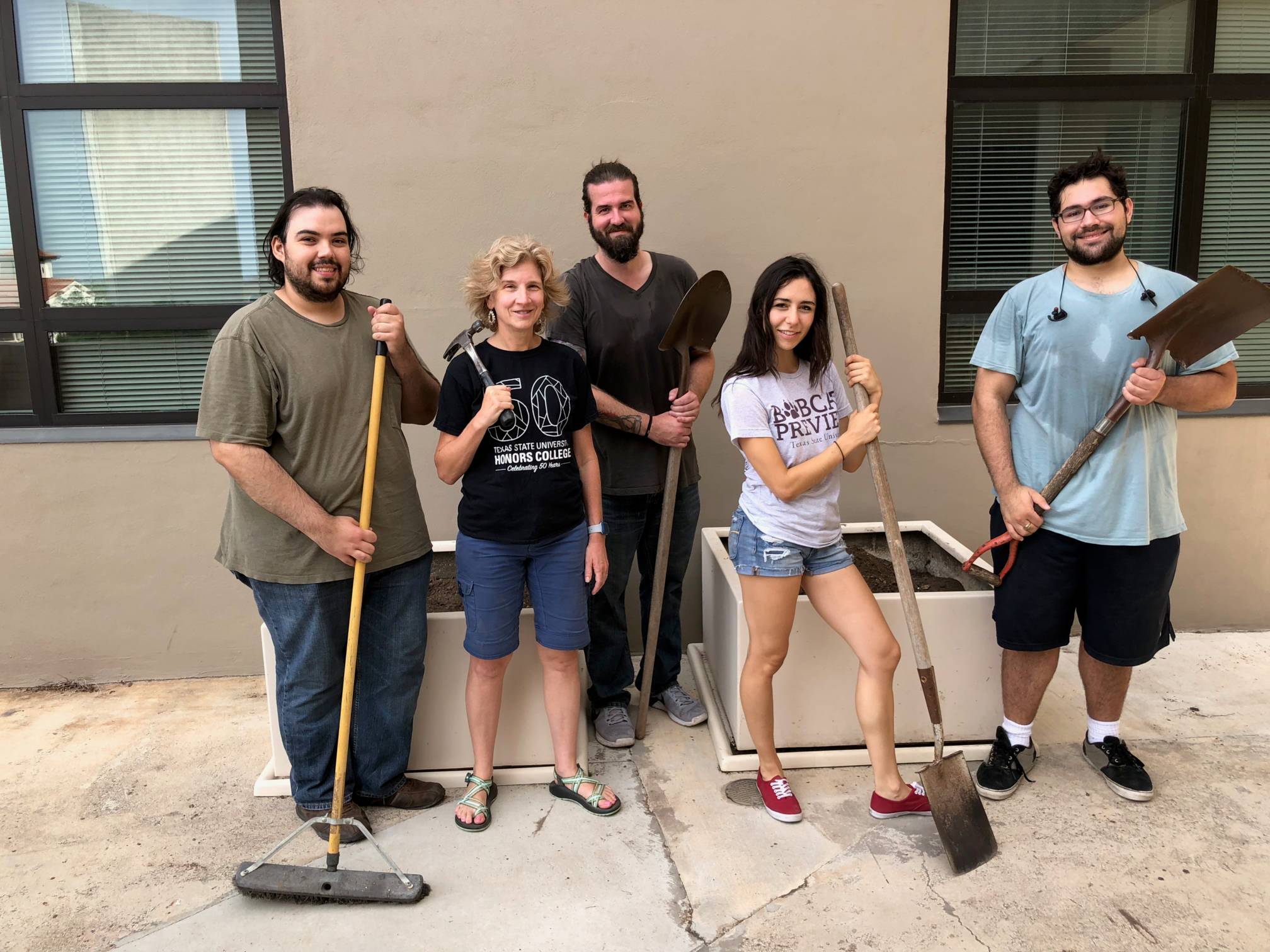 three men and two women pose with shovels and brooms