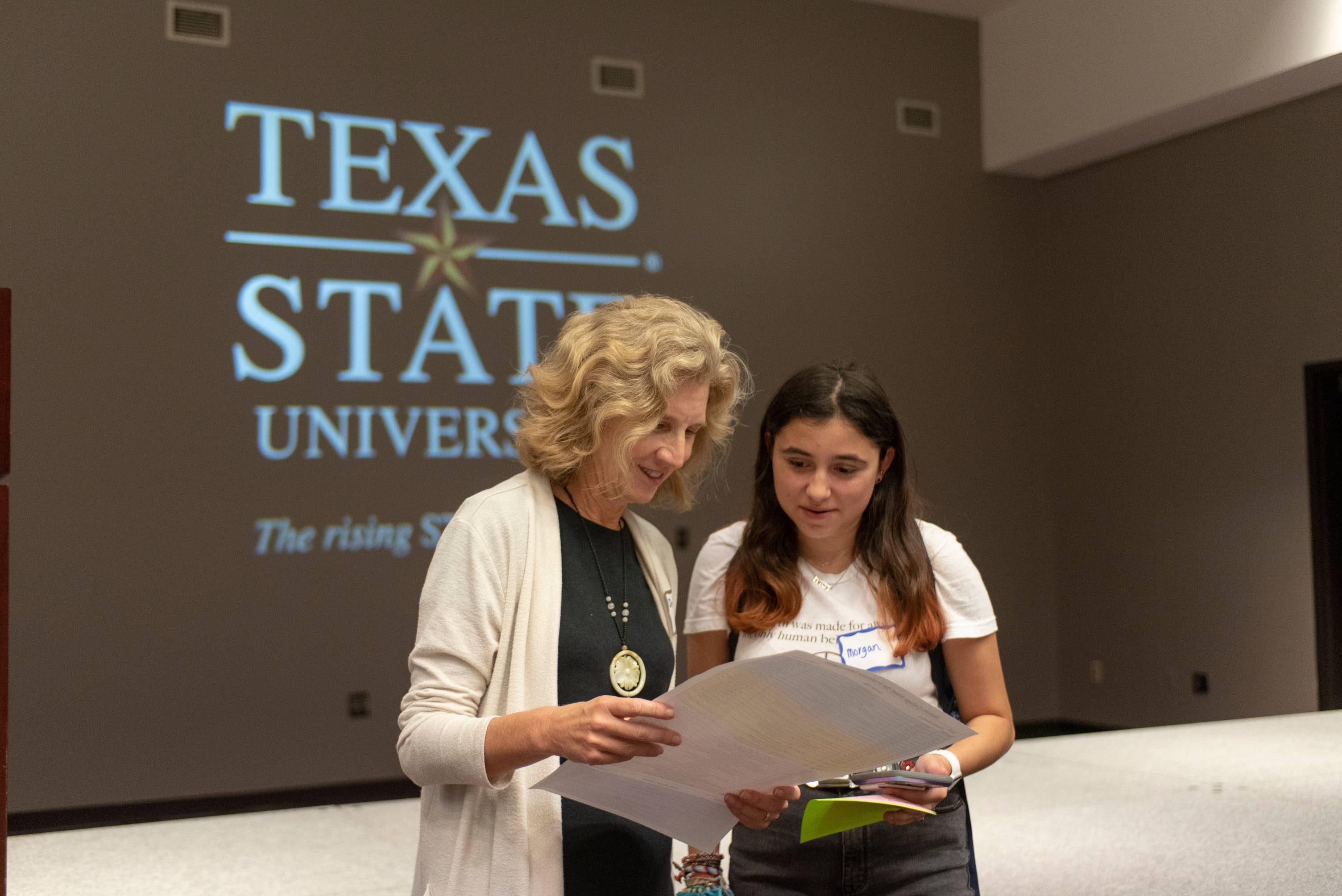 Dean Galloway looks at poster with female student in front of Texas State University sign
