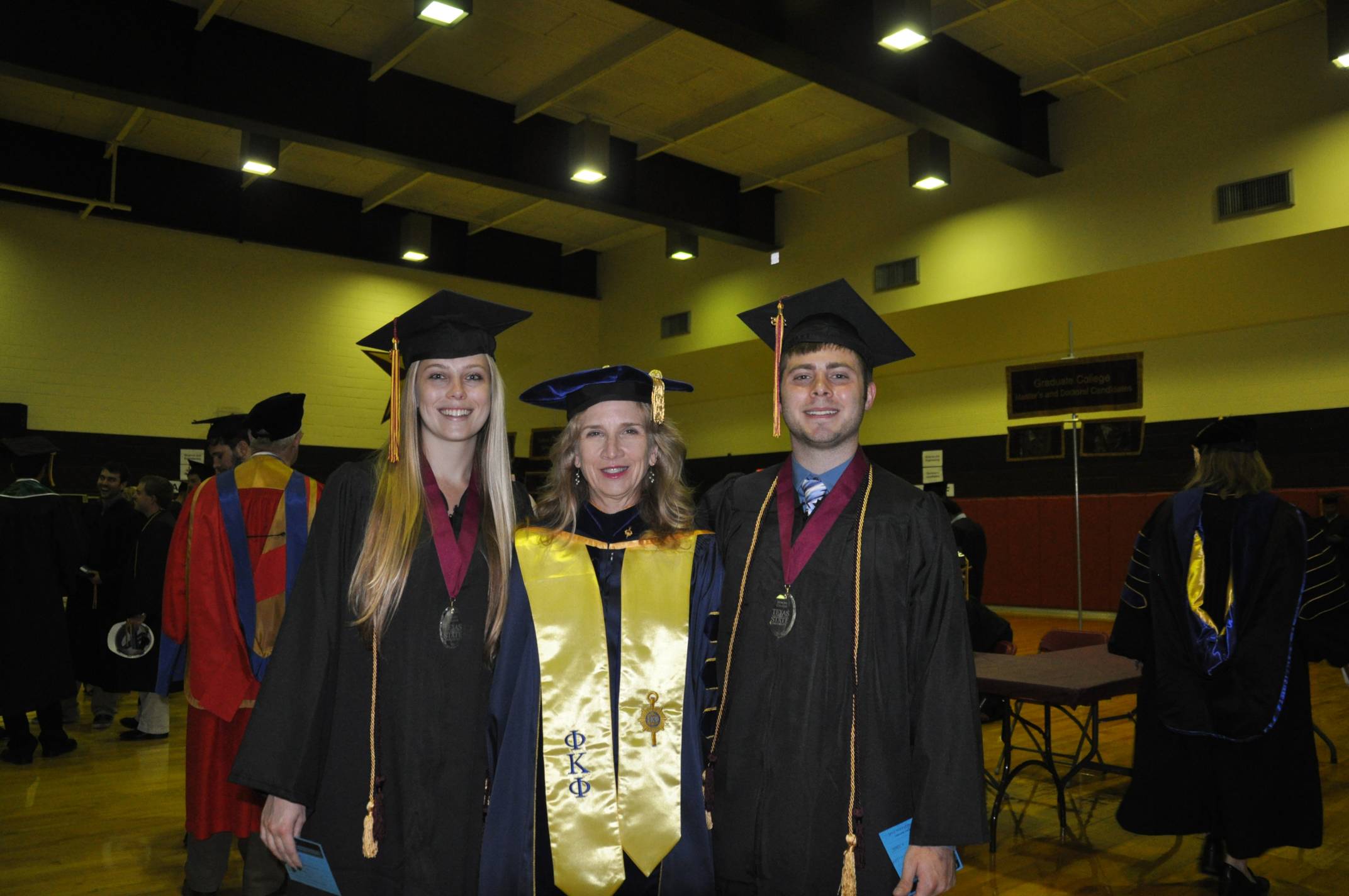 dean galloway with two honors college graduates. all are wearing graduation regalia