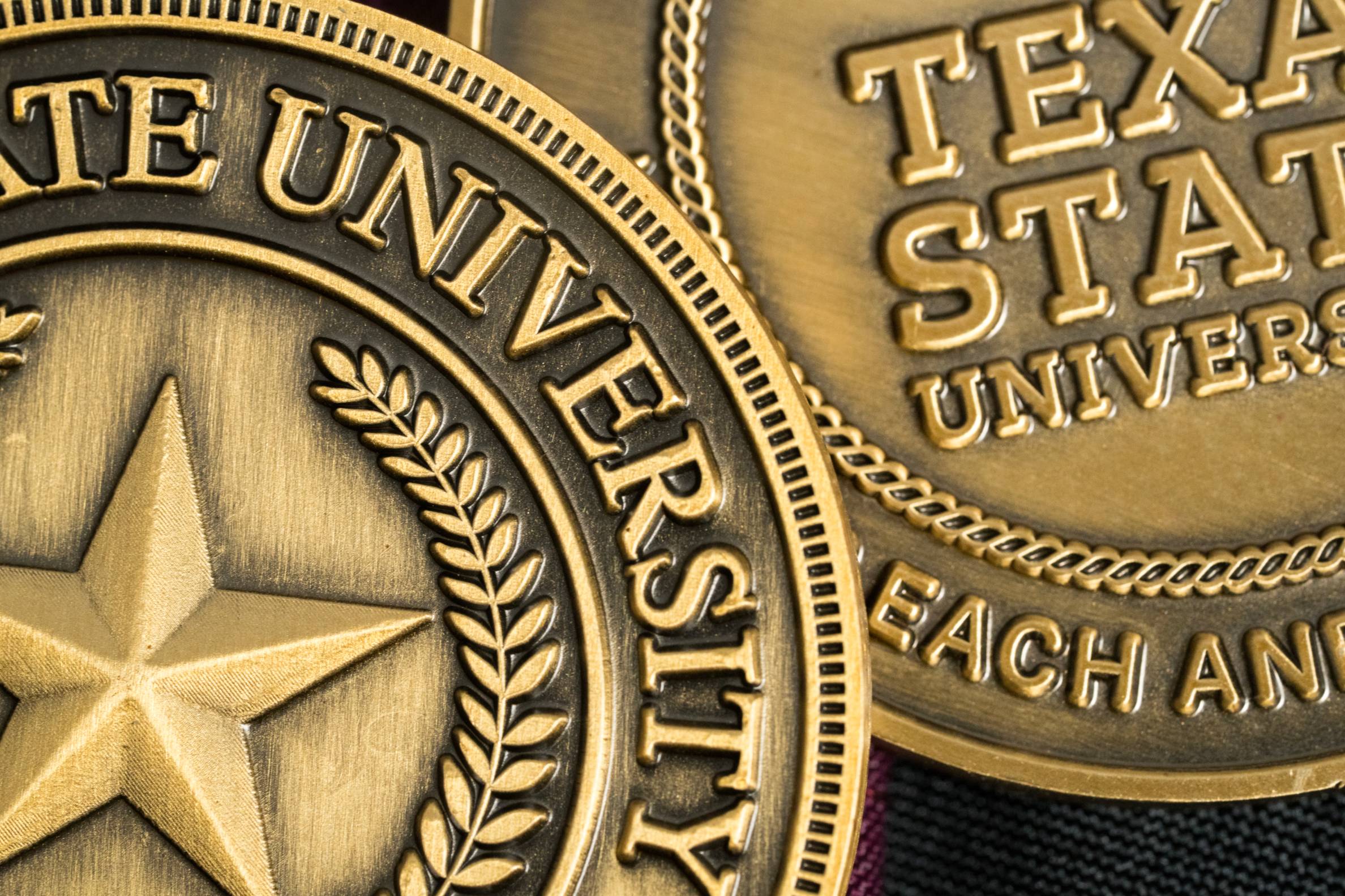 close up of two challenge coins with the current and previous TXST logos