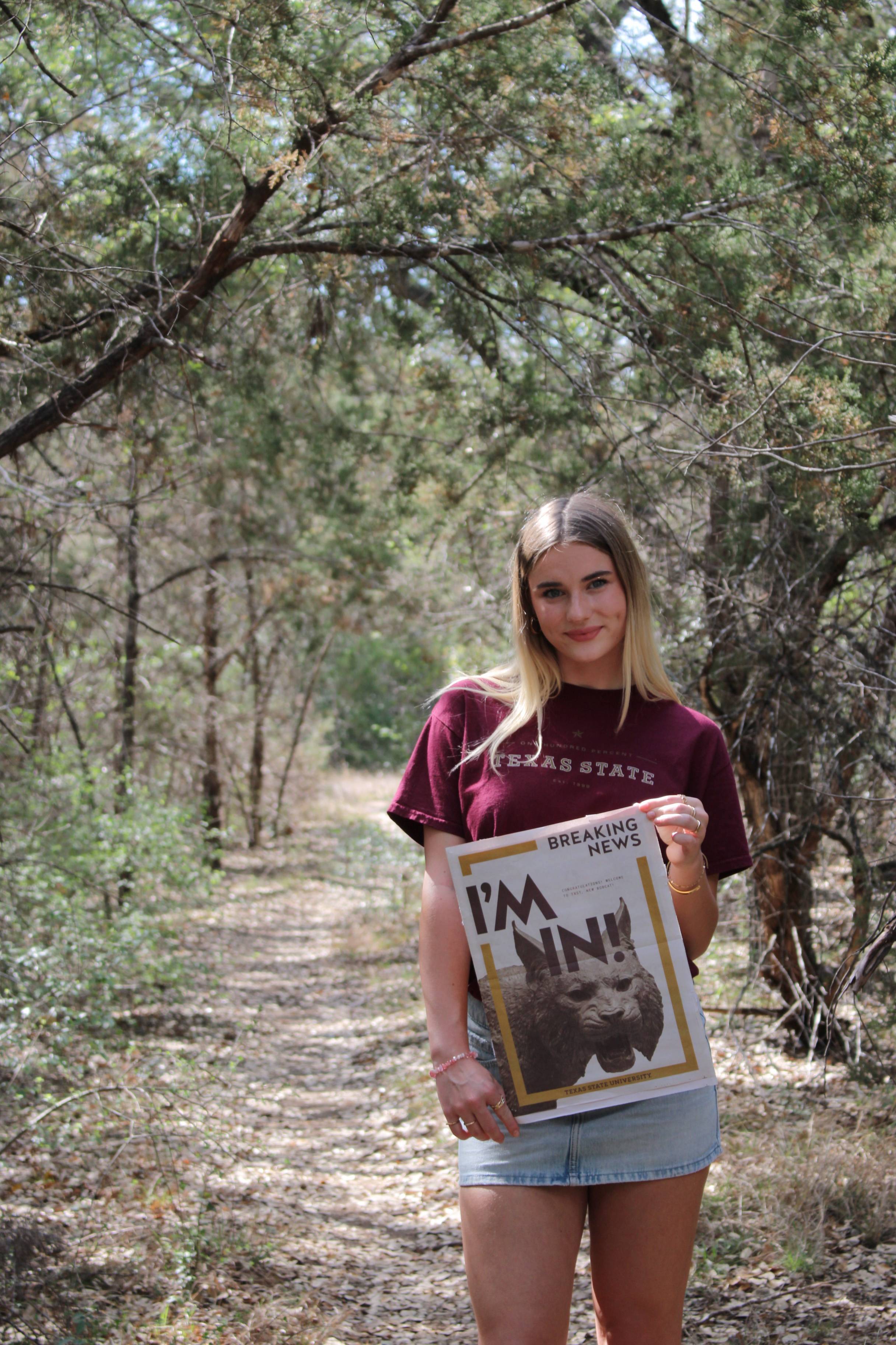woman standing in hiking trail while holding a newspaper that reads "I'm in!"