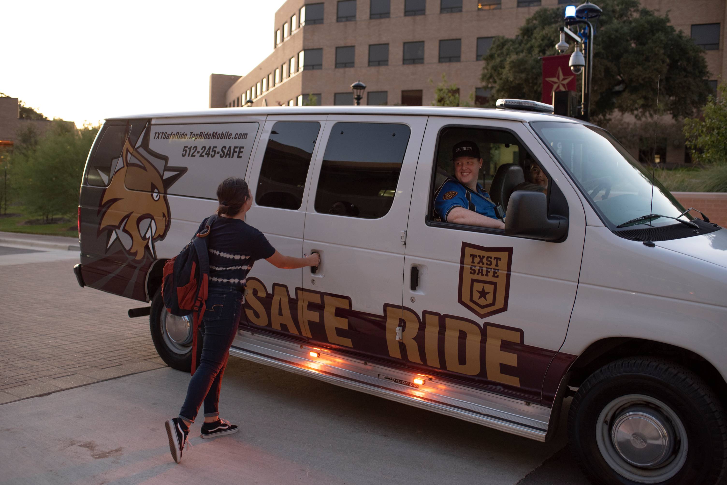 woman holding onto car handle of big van that reads "Safe Ride"