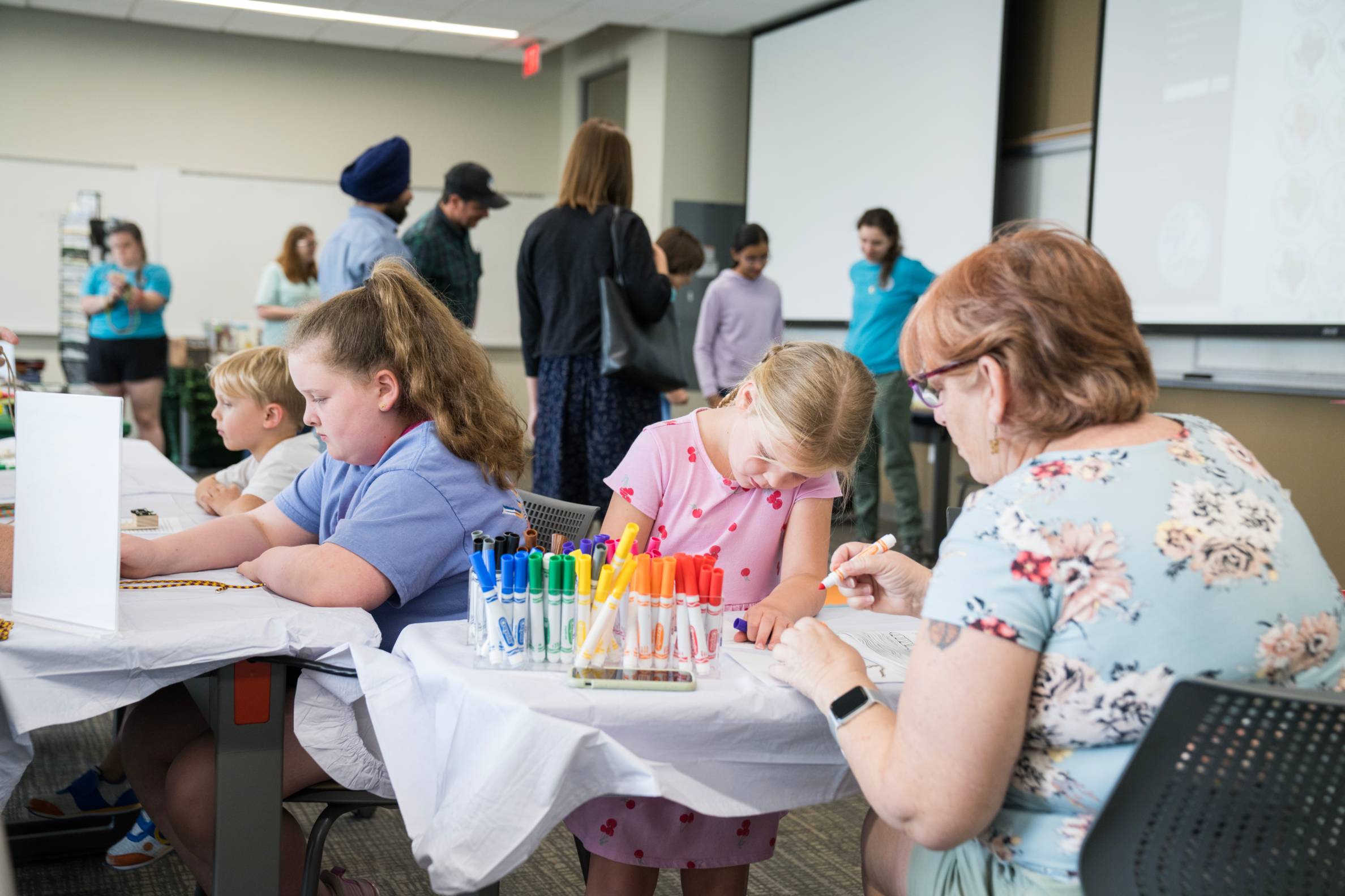 multiple kids and an adult color with markers at different tables