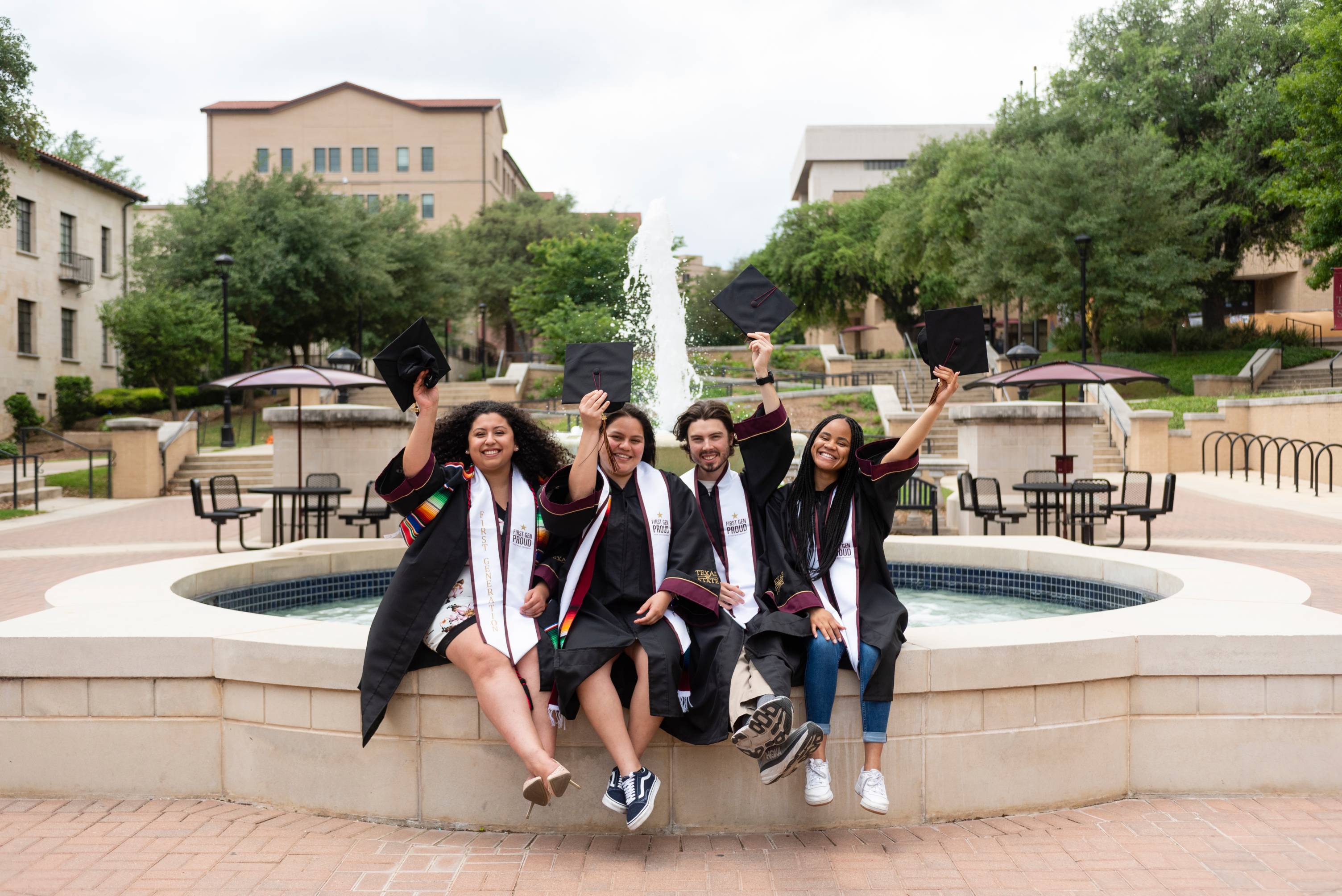 Four bobcats sit on the edge of the Bobcat Trail fountain, hands rasied in celebration