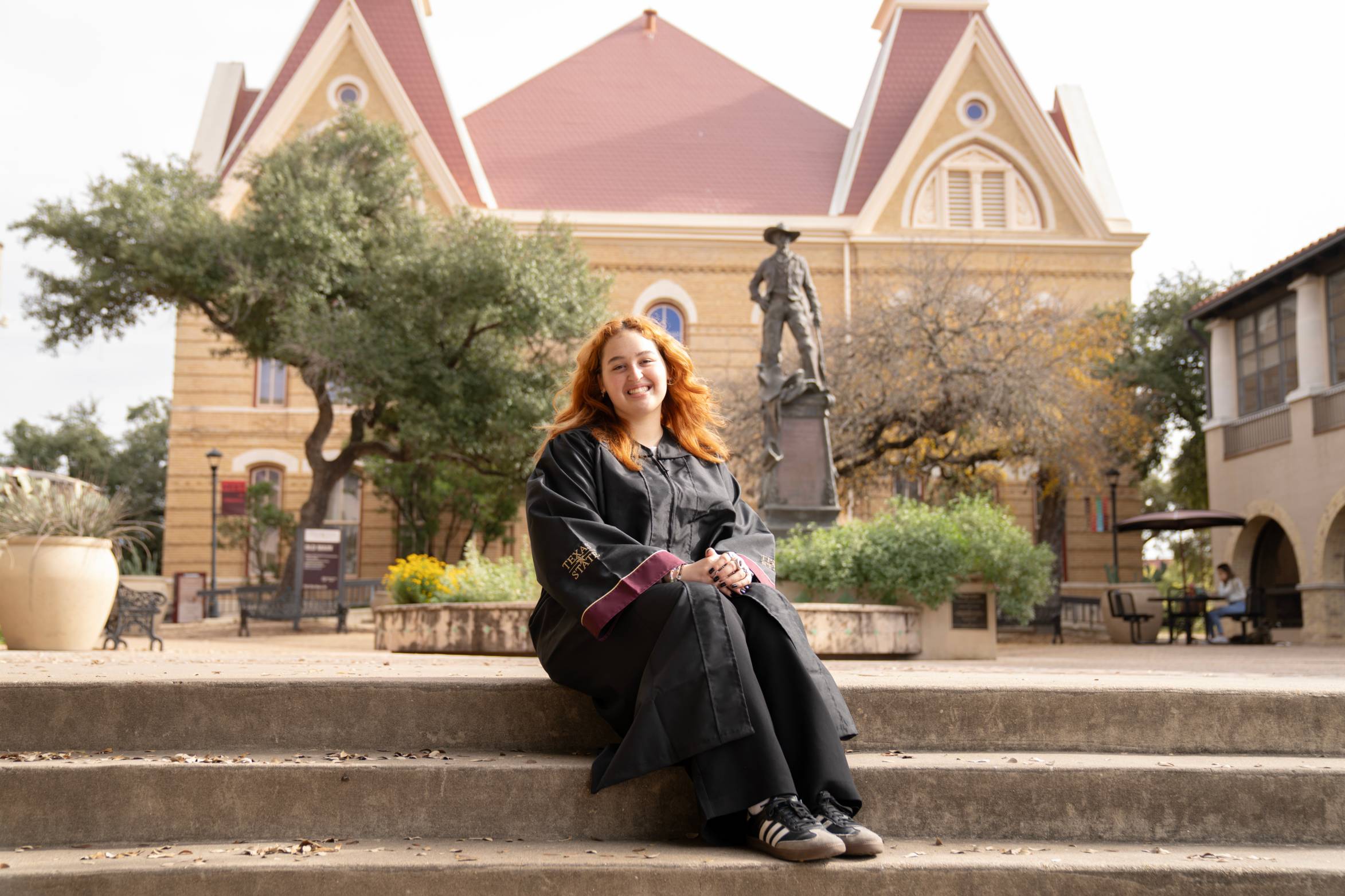 A graduate sits on the steps of Old Main, smiling at the camera