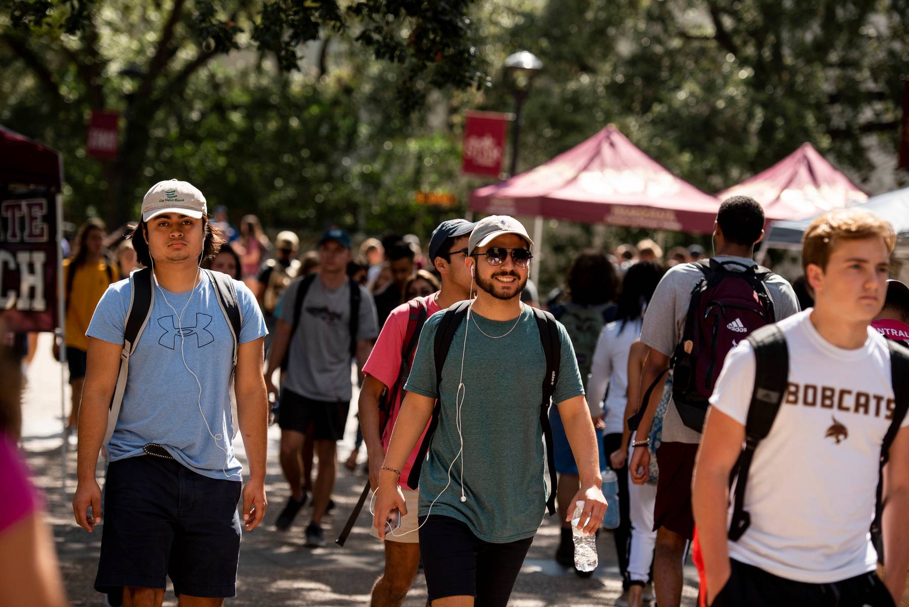 a crowd of students walking with vendor tents set up in the background