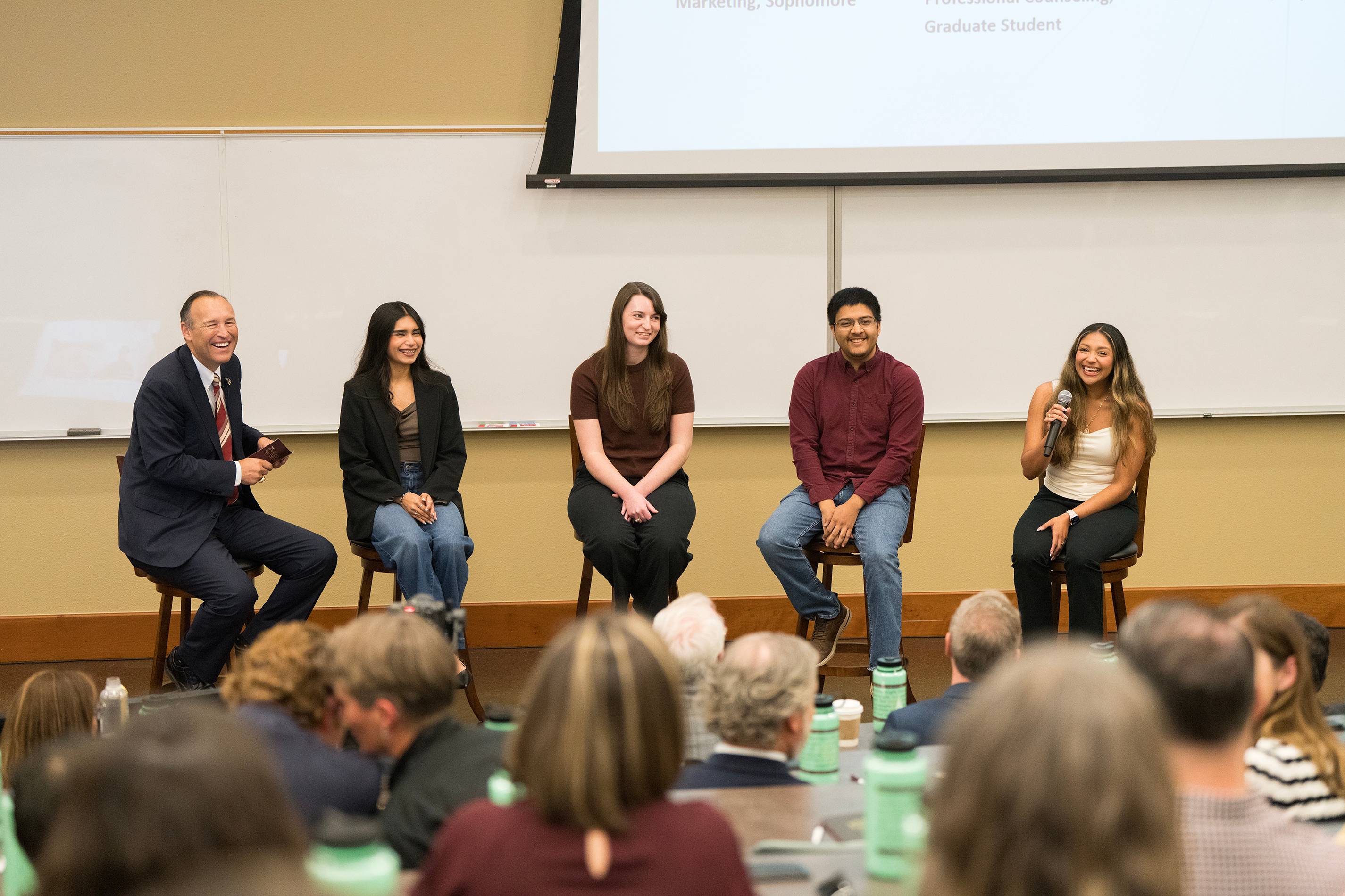 five people participating in a panel in front of a large audience