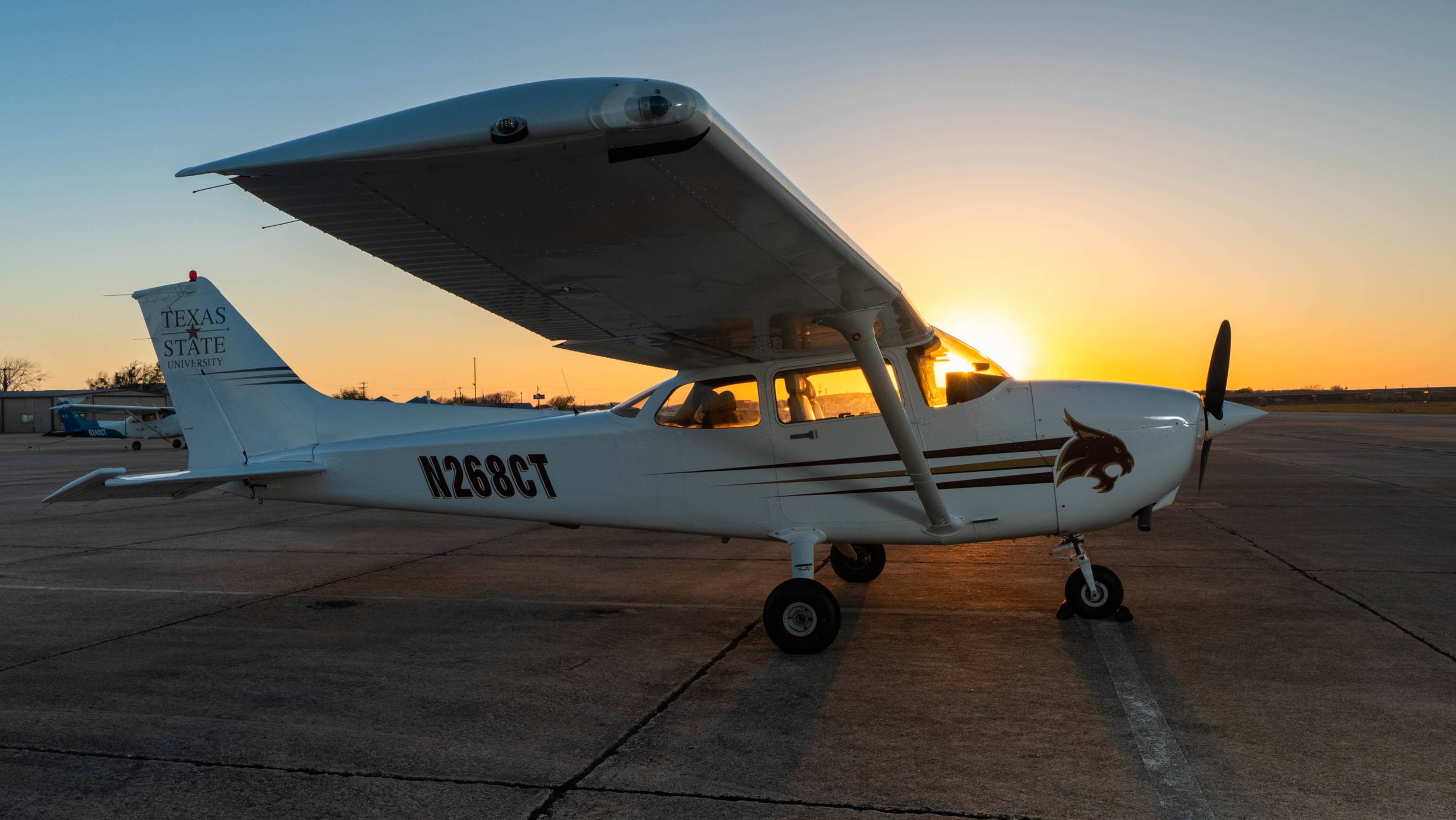 a TXST biplane sits on the tarmac at sunset
