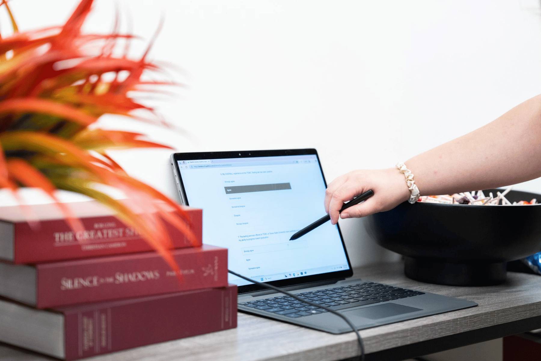 Books and a laptop with a person's hand pointing at the screen.