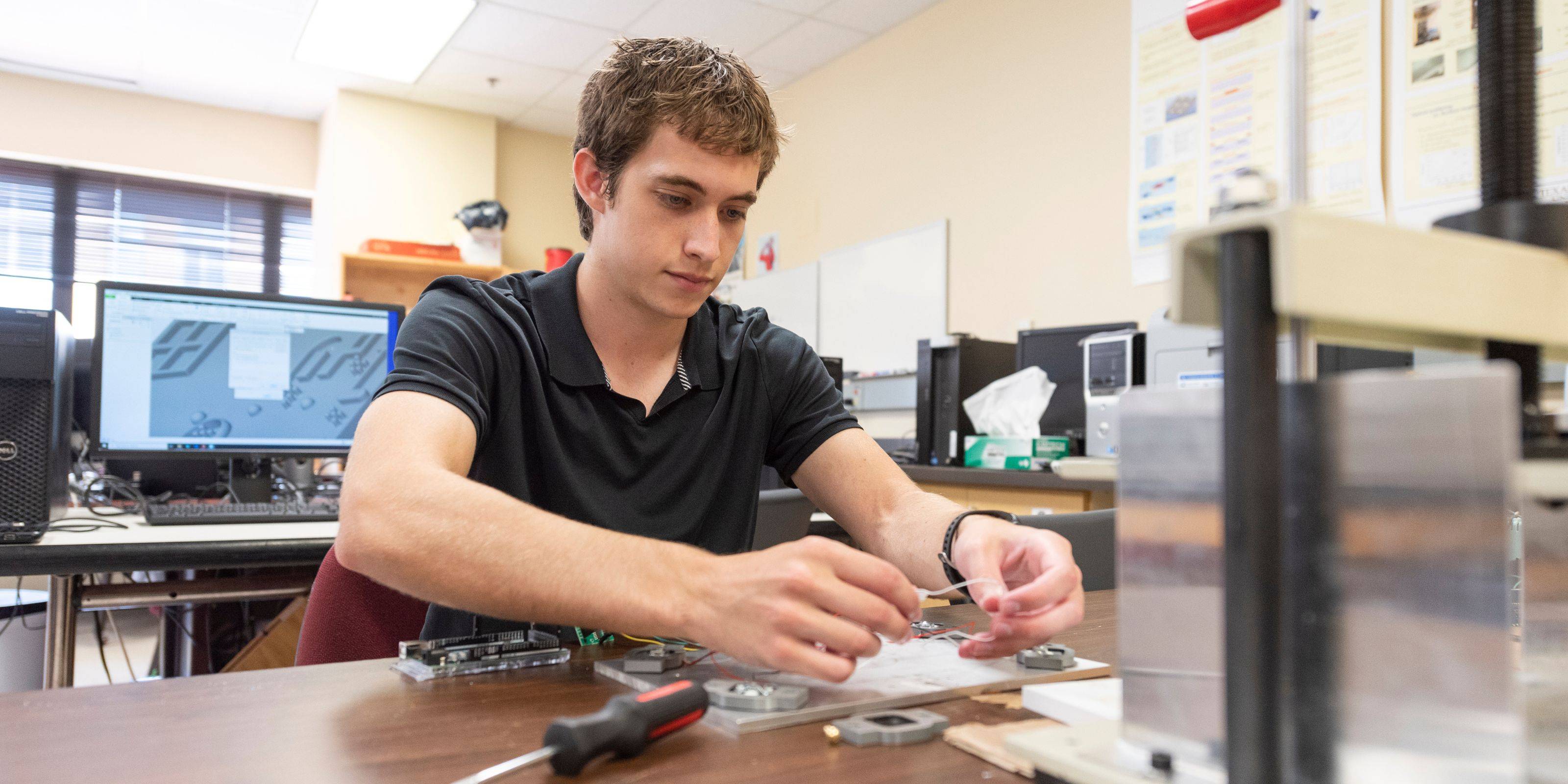 A student welding a piece of metal while sitting at a table