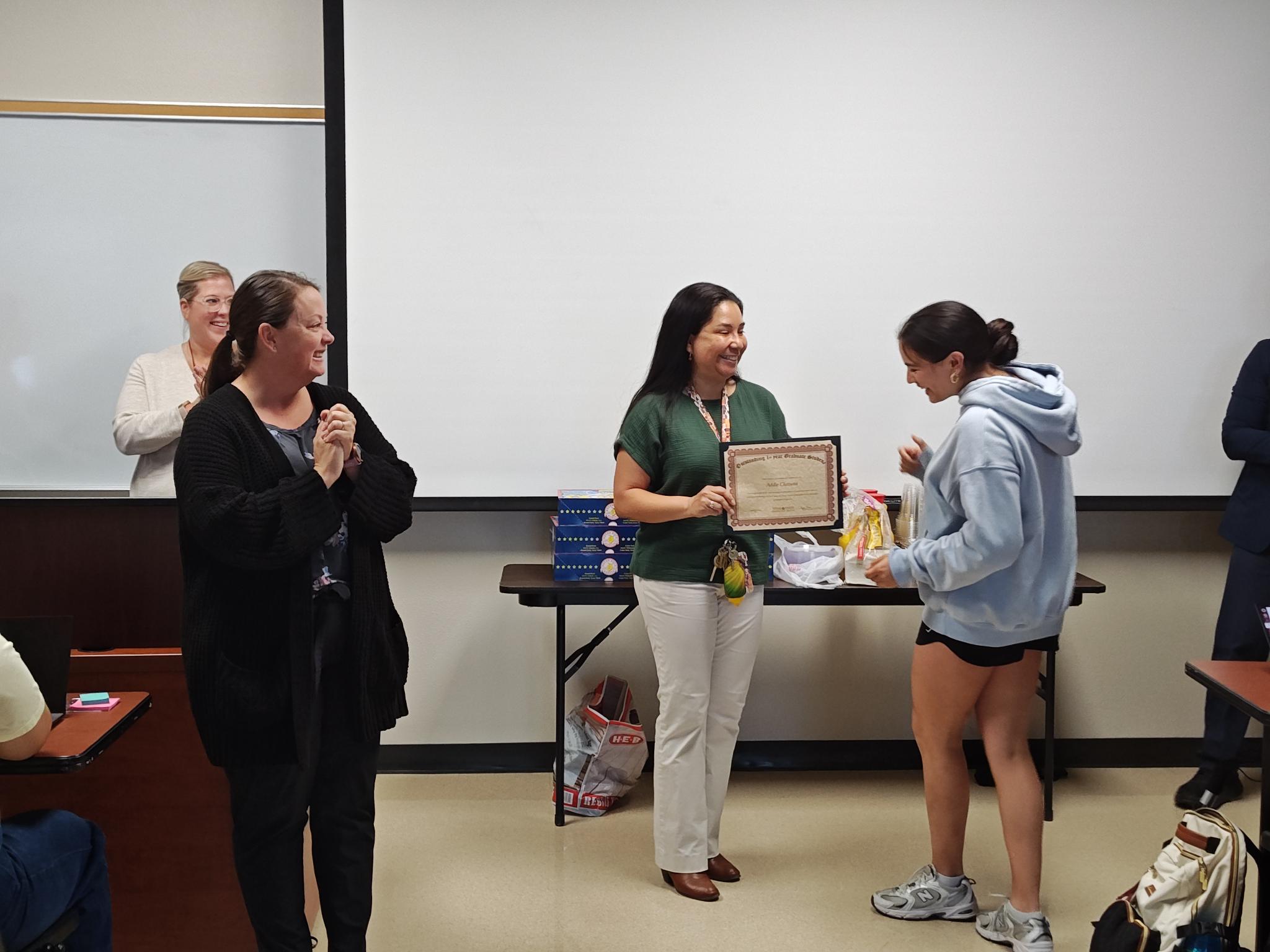 1st Year Graduate Student receiving a diploma from the hands of Dr. Maria Resendiz and other CDIS faculty members are applauding.