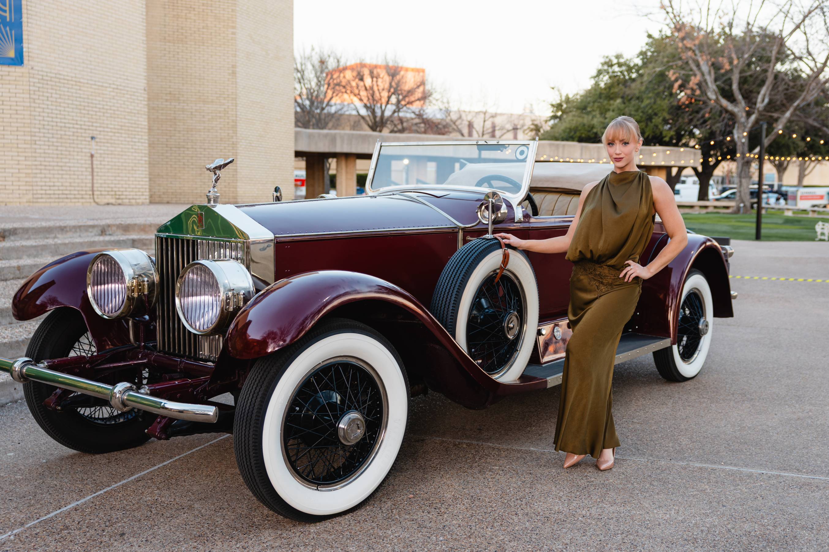 woman wearing ballgown stands next to vintage maroon car
