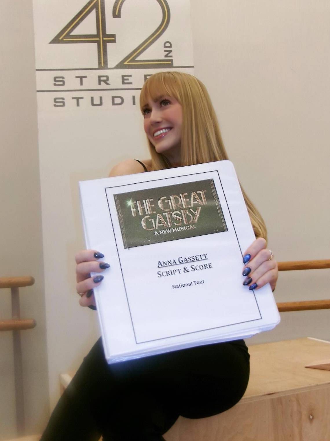 woman sits while holding up a white binder that contains her script for The Great Gatsby on Broadway
