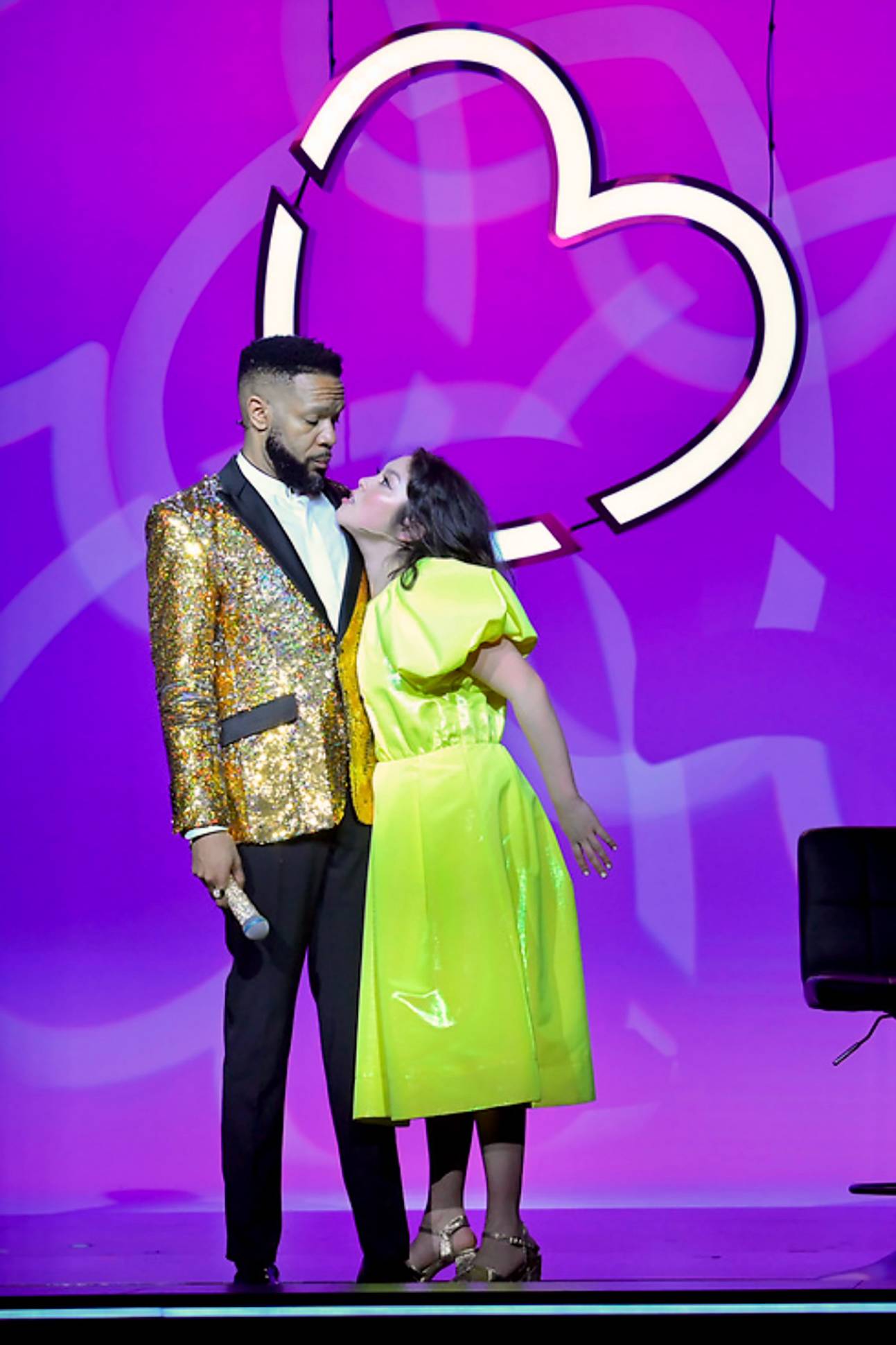 woman in bright green dress looks up at man in sparkly gold blazer