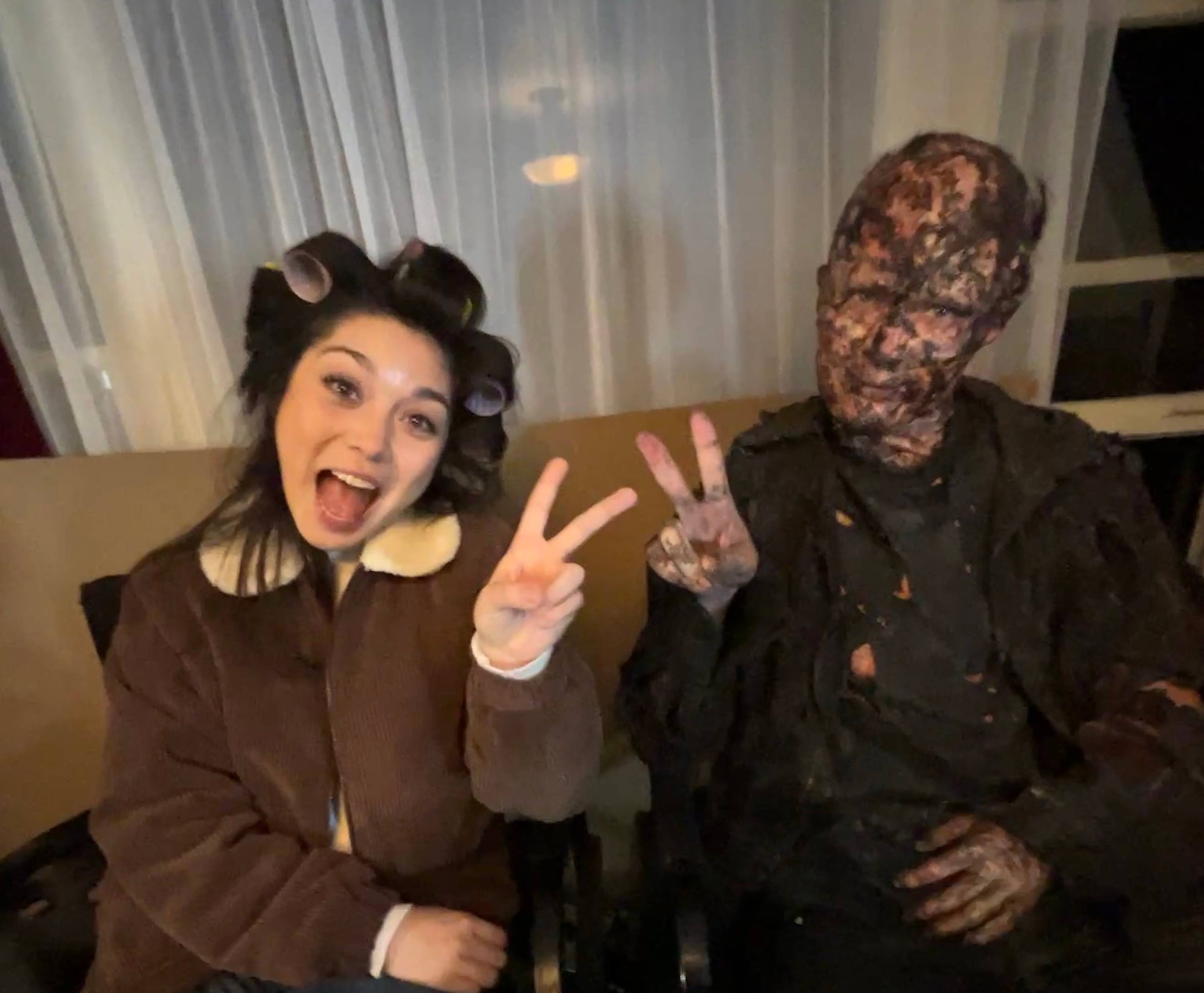 anna yi puig poses for photo with man in special effects make up. they are holding up peace signs
