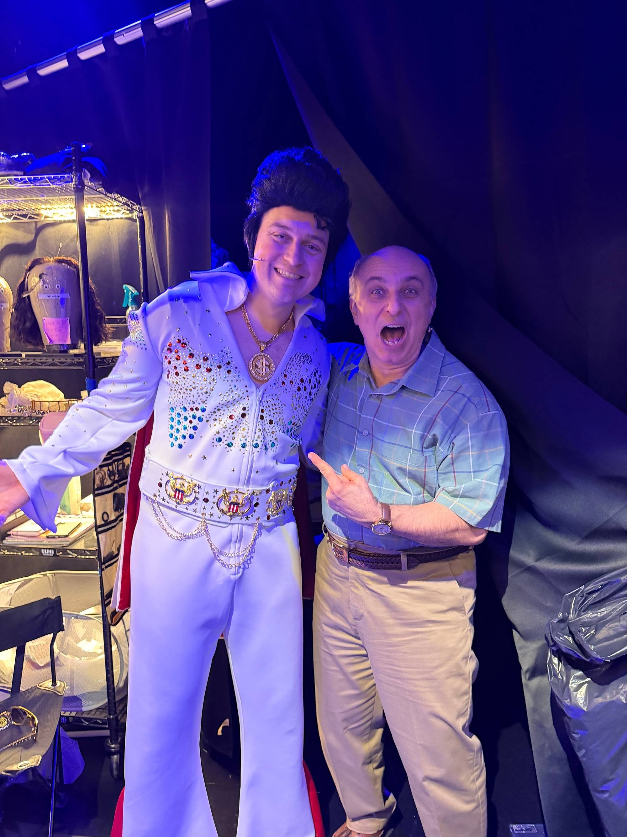 man in an elvis costume poses for a photo with another man. the other man is pointing at elvis with an excited look on his face.