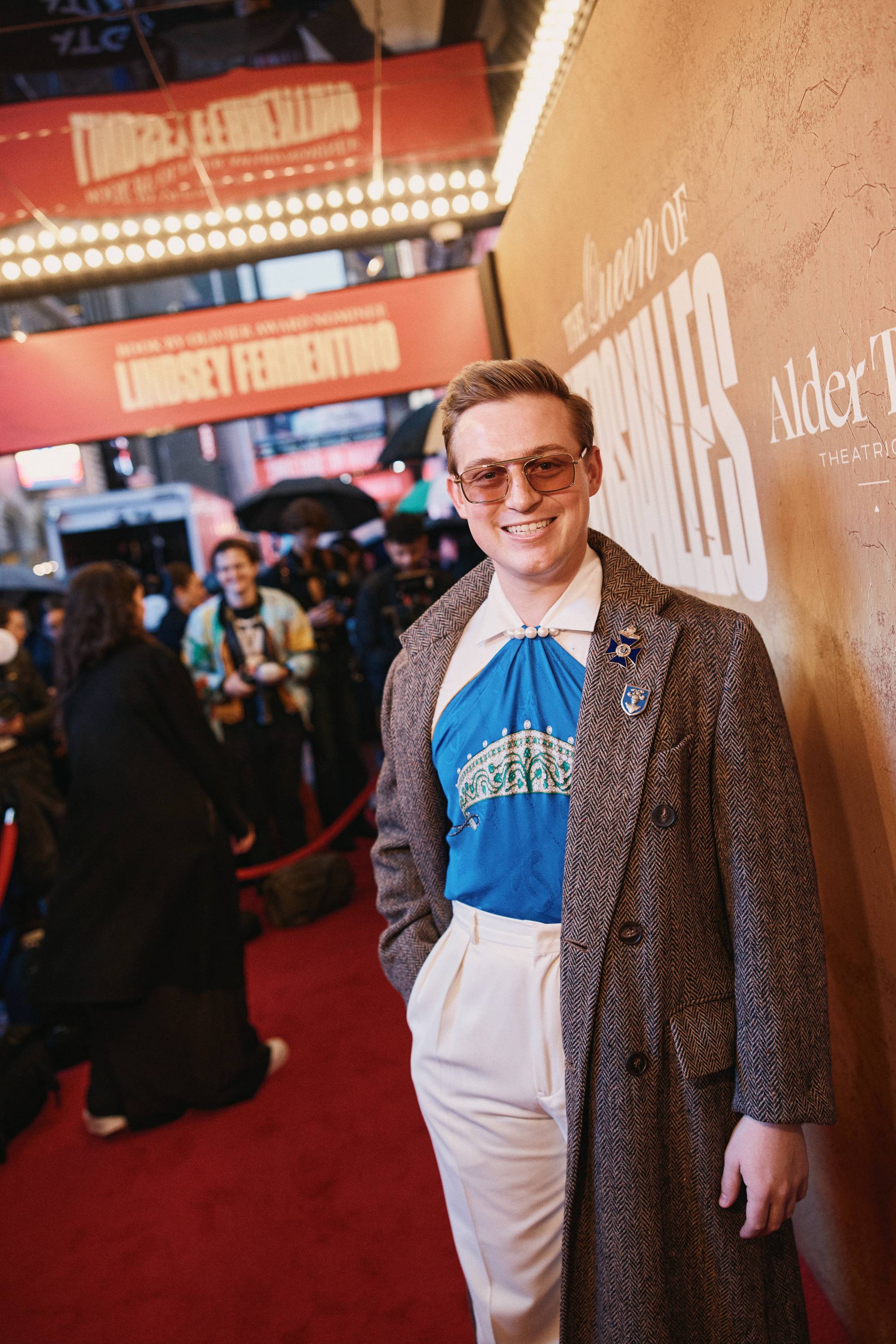 jake young standing on a red carpet wearing a long brown coat