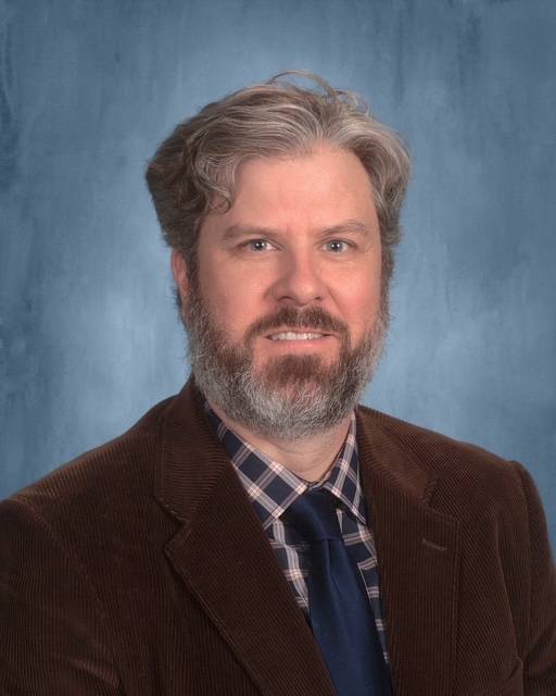 Man with gray hair and goatee in a suit smiling at camera