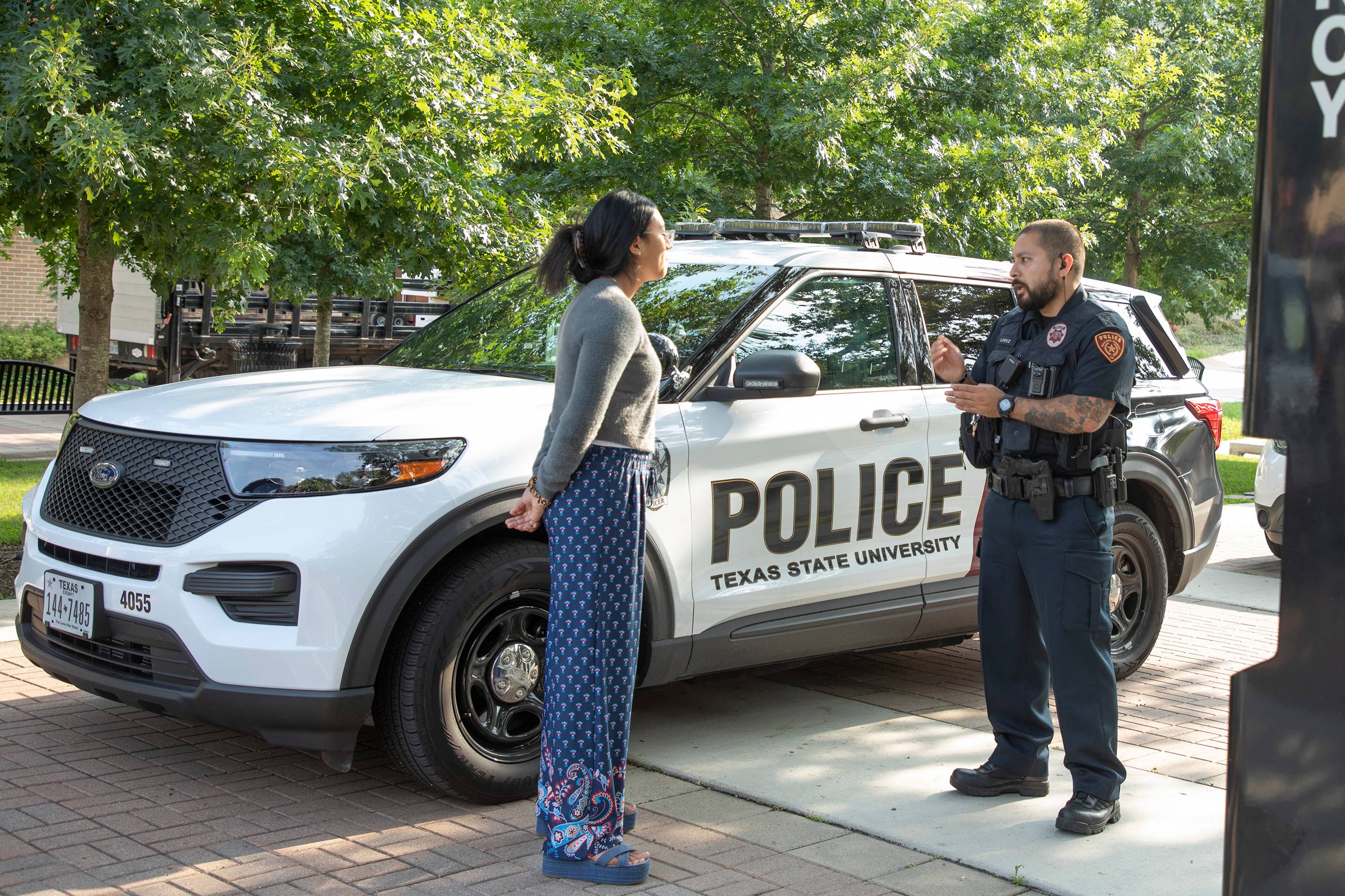 woman speaking to man in police uniform next to white police SUV