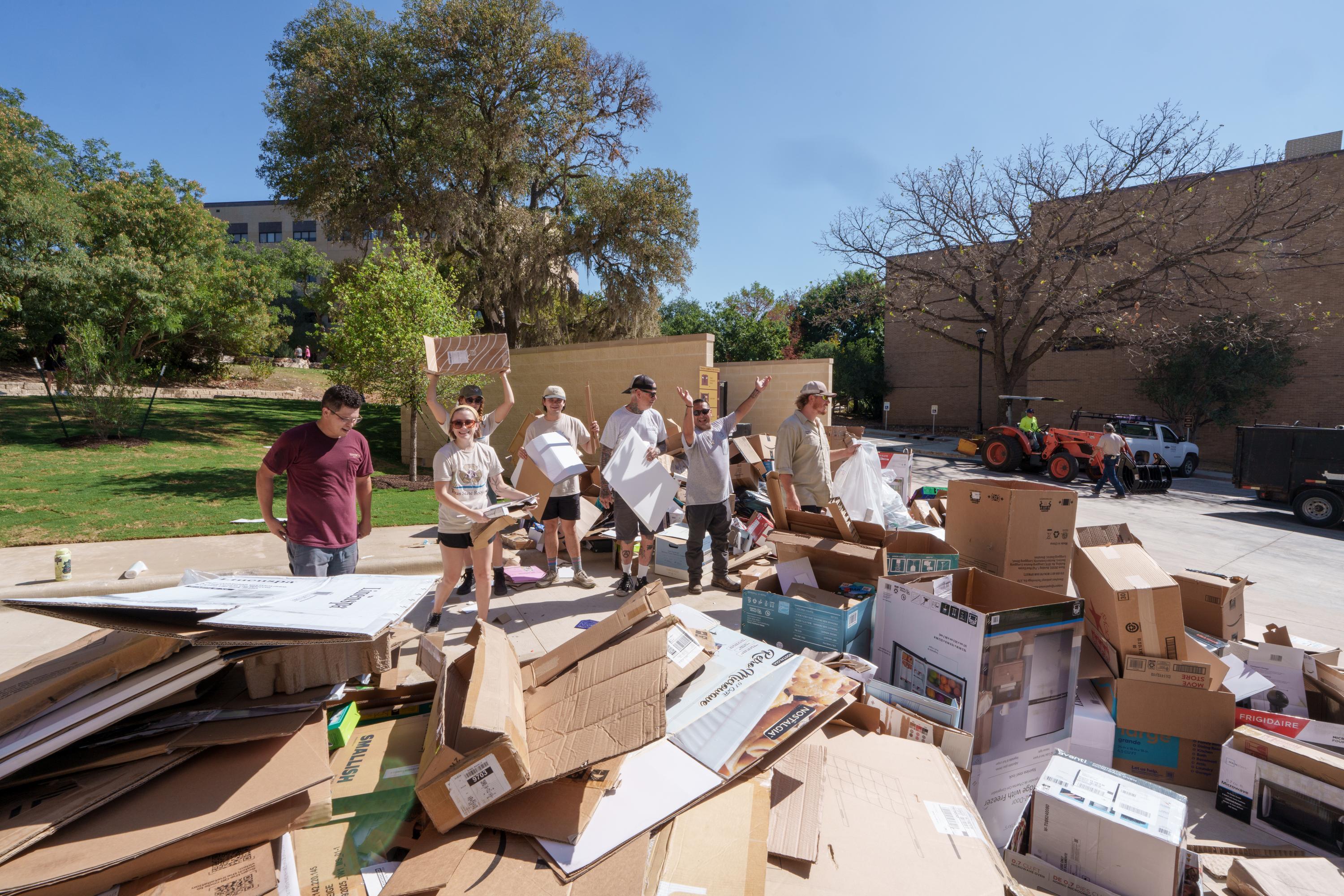 group of people standing behind a large pile of broken down cardboard boxes