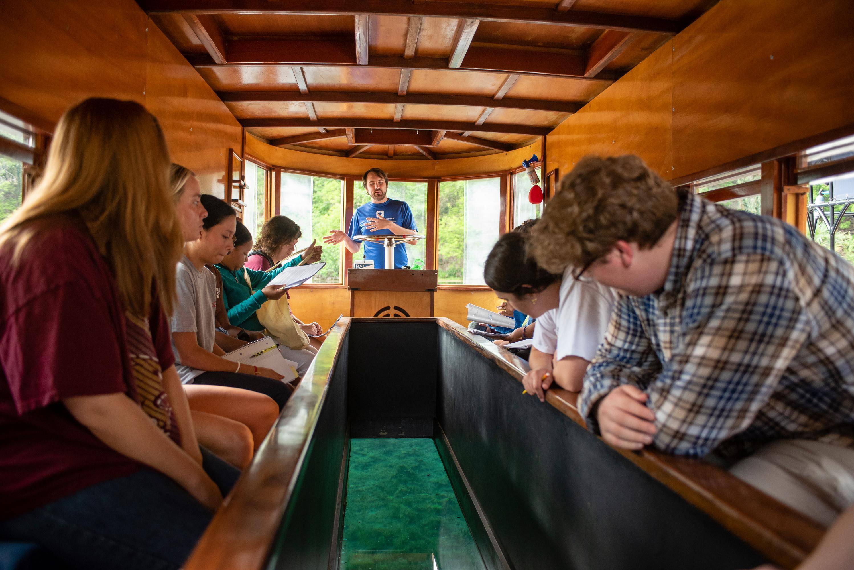 people in a wooden boat looking down at the lake through the boat's glass bottom