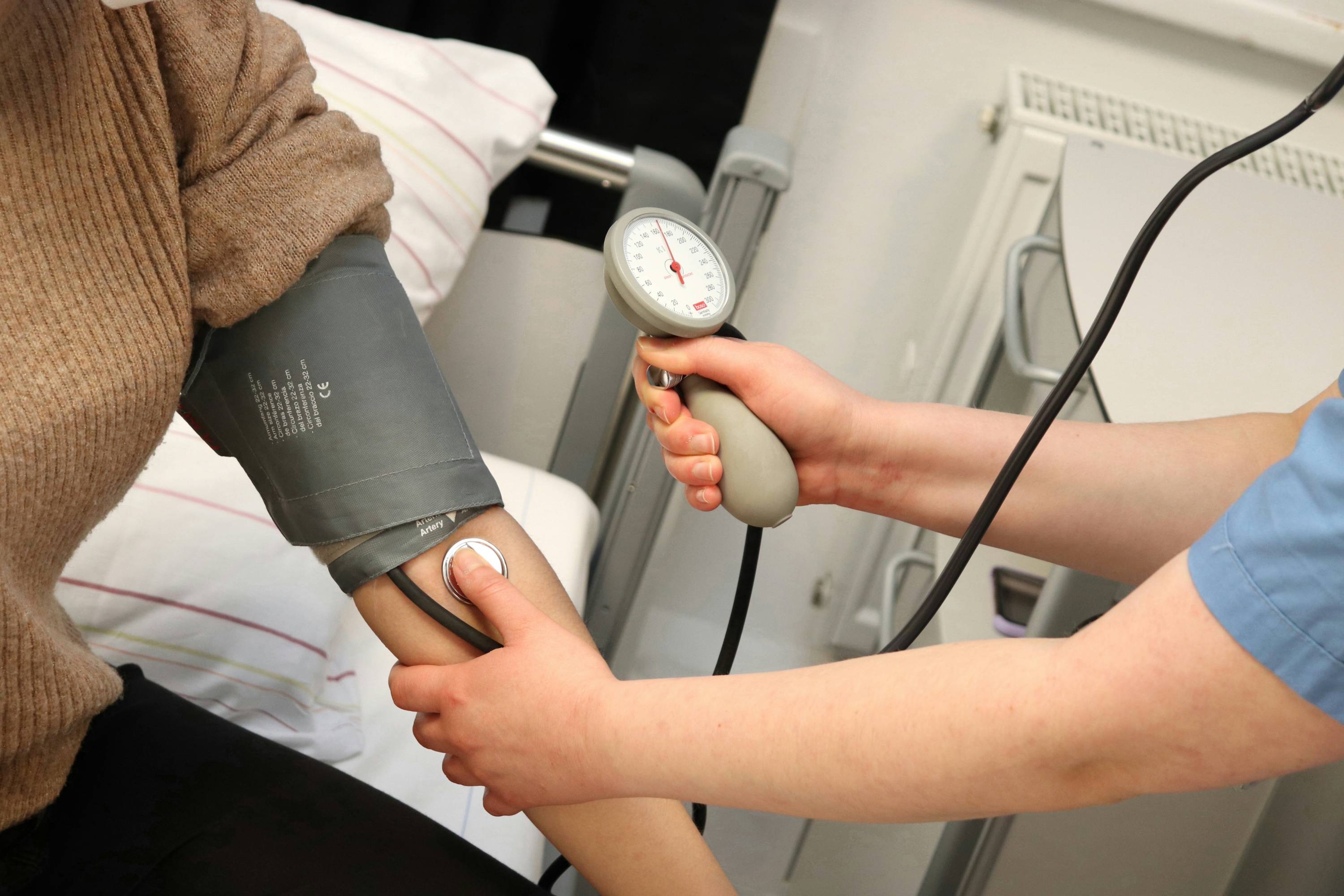 Healthcare professional checking a patient’s blood pressure with a manual cuff and stethoscope in a clinical setting.