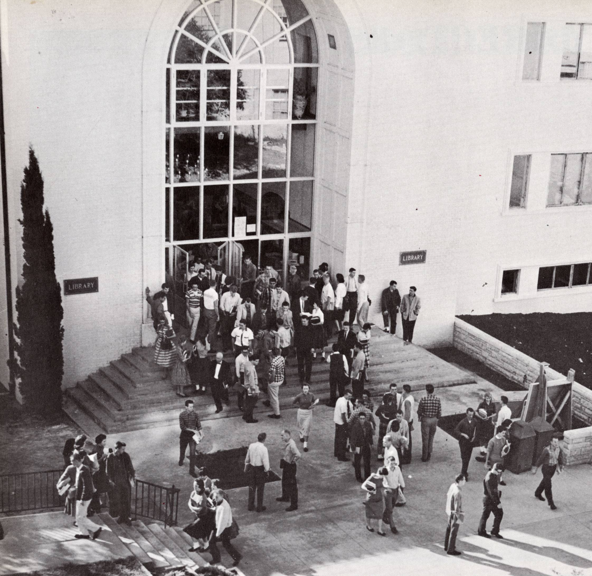 A black and white picture of people outside a building