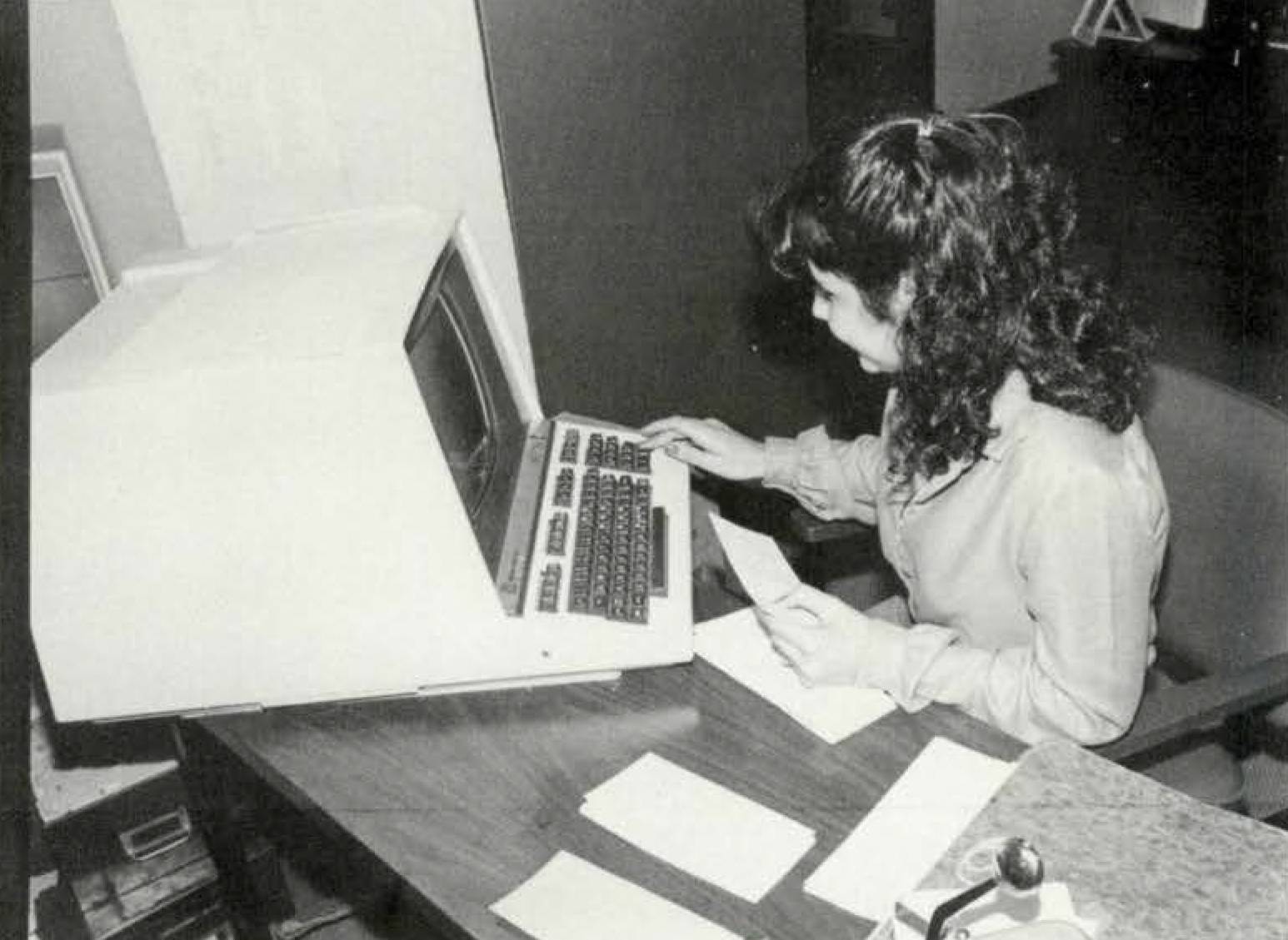 A black and white picture of a woman using an old computer 