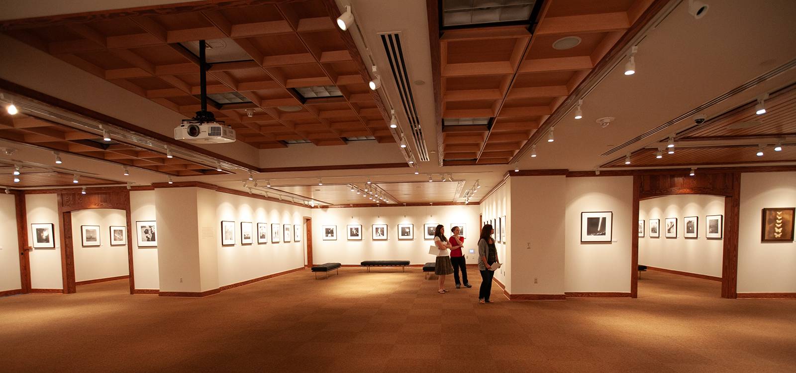 People wander through a large gallery with photographs along the wall.