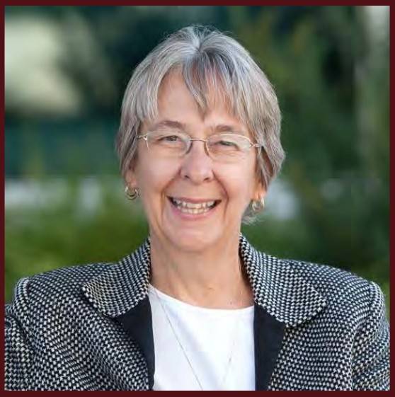 Dr. Hailey with glasses outdoors in front of greenery
