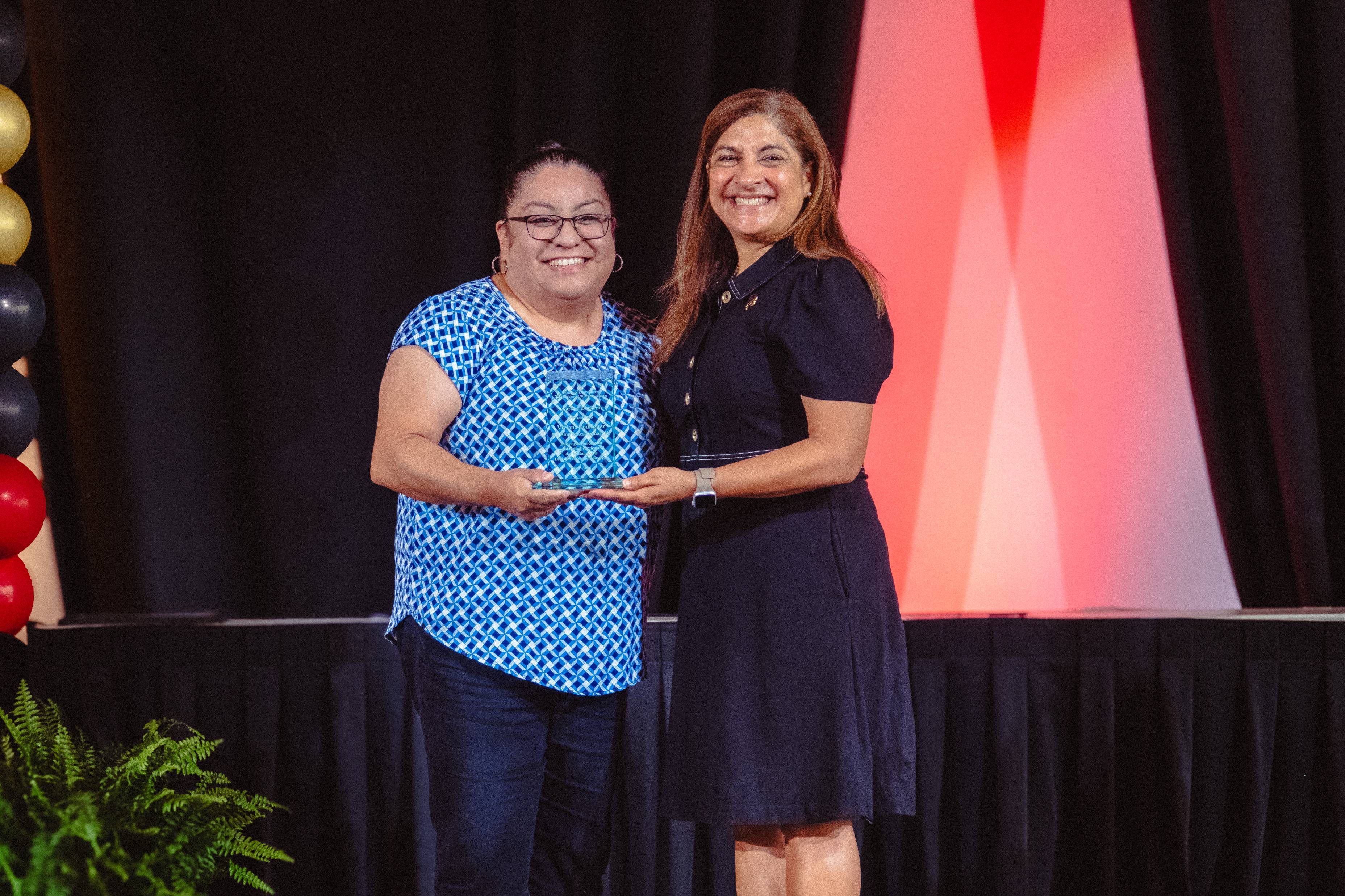 Viviana Rodriguez and Dr. Cynthia L. Hernandez Hold an award on stage 