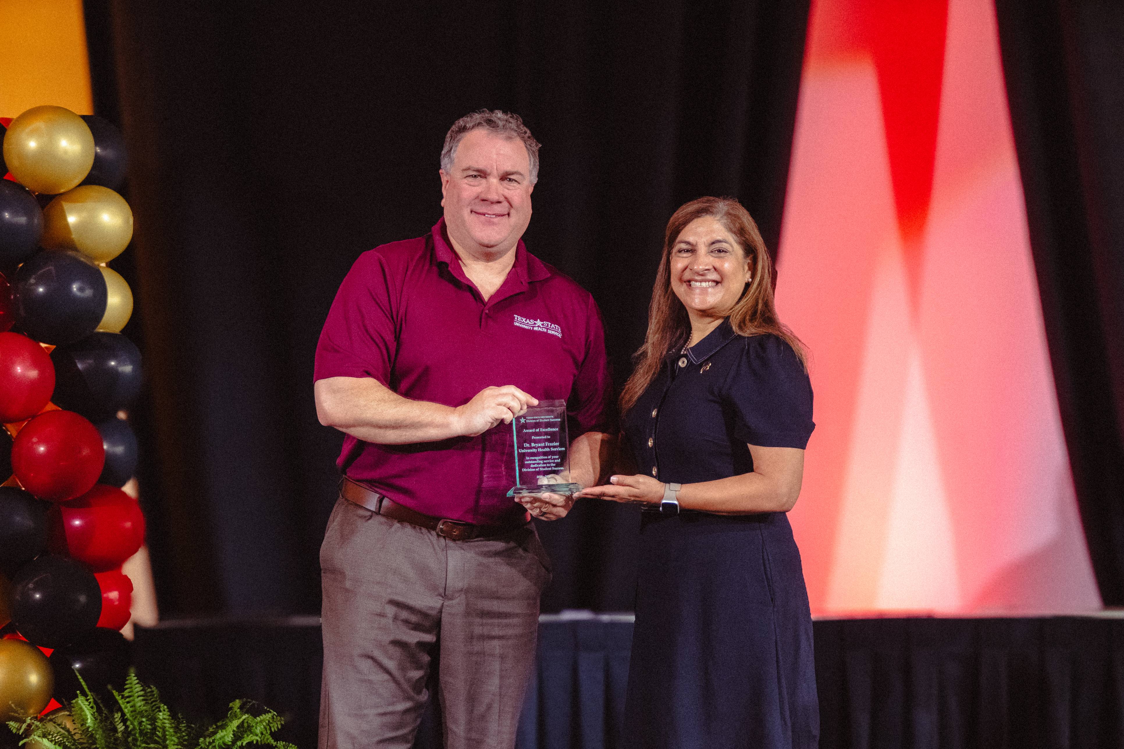 Dr. Bryant Frazier and Dr. Cynthia L. Hernandez Hold an award on stage 